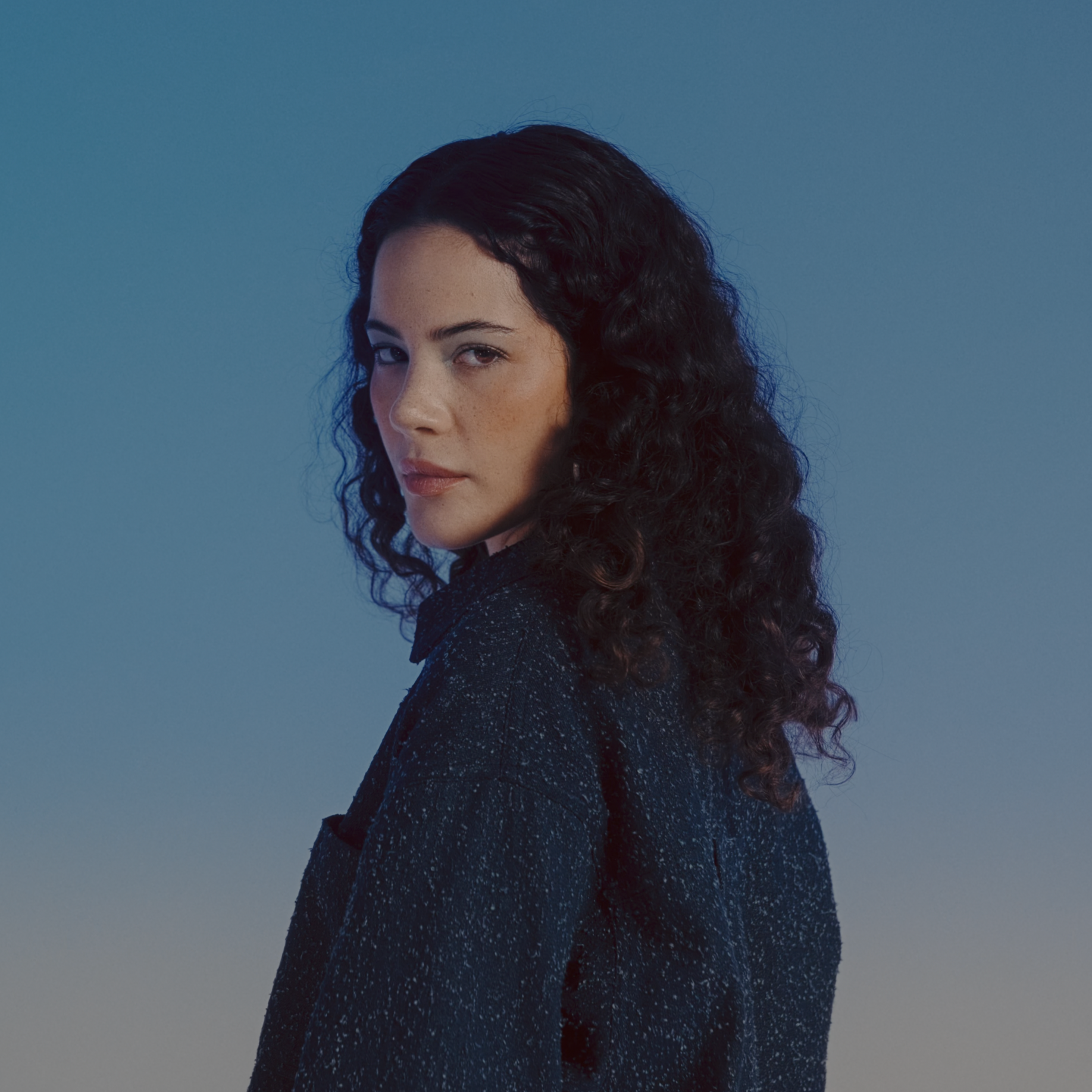 Retrato de una mujer con cabello rizado y oscuro, usando un vestido negro, en un fondo azul. Video de moda.