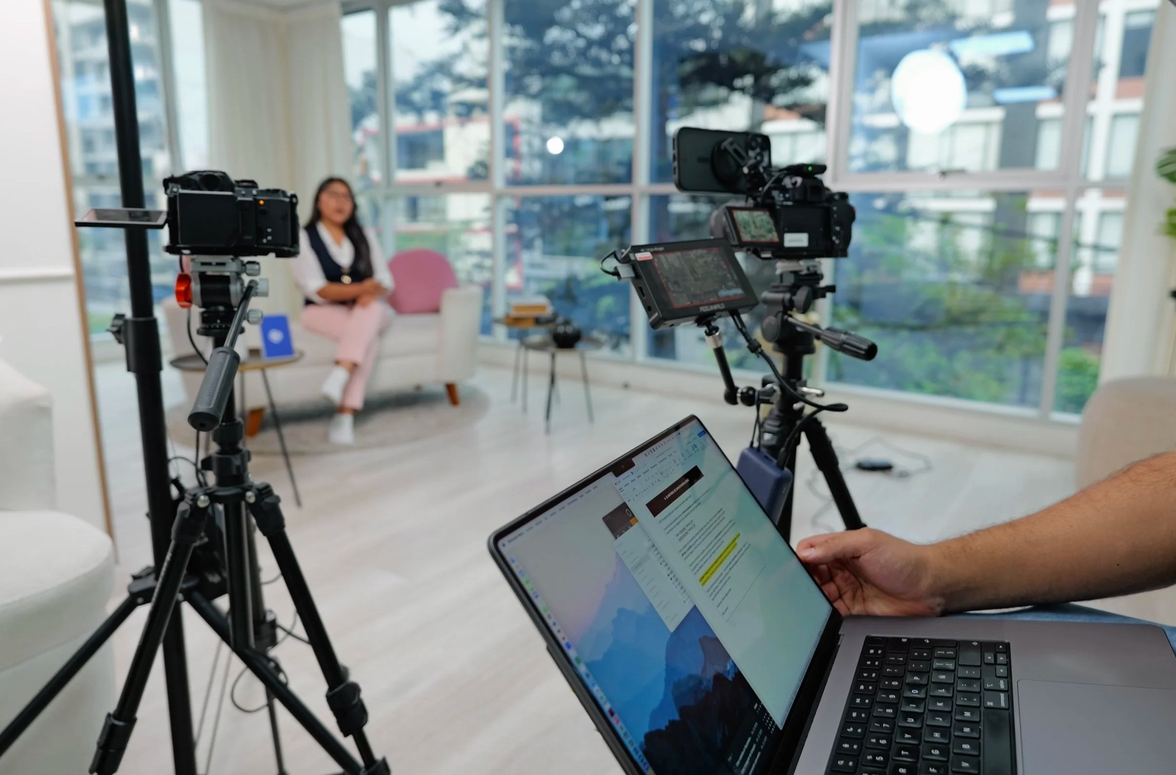 Un estudio de grabación con una mujer sentada en un sillón y varias cámaras apuntando hacia ella, mientras un técnico trabaja en una laptop en primer plano.