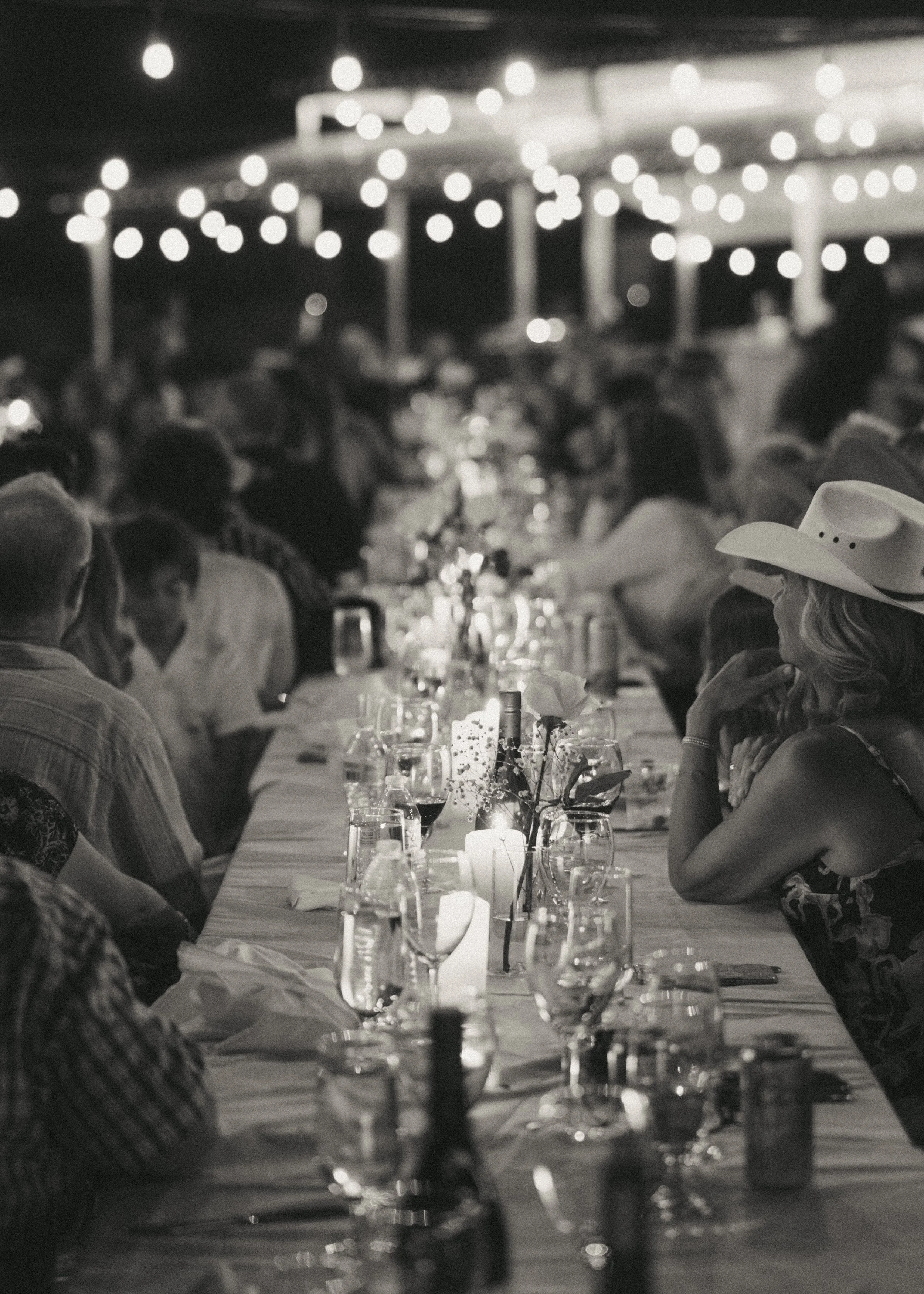 People gathered at a long dinner table under string lights during an outdoor evening event.