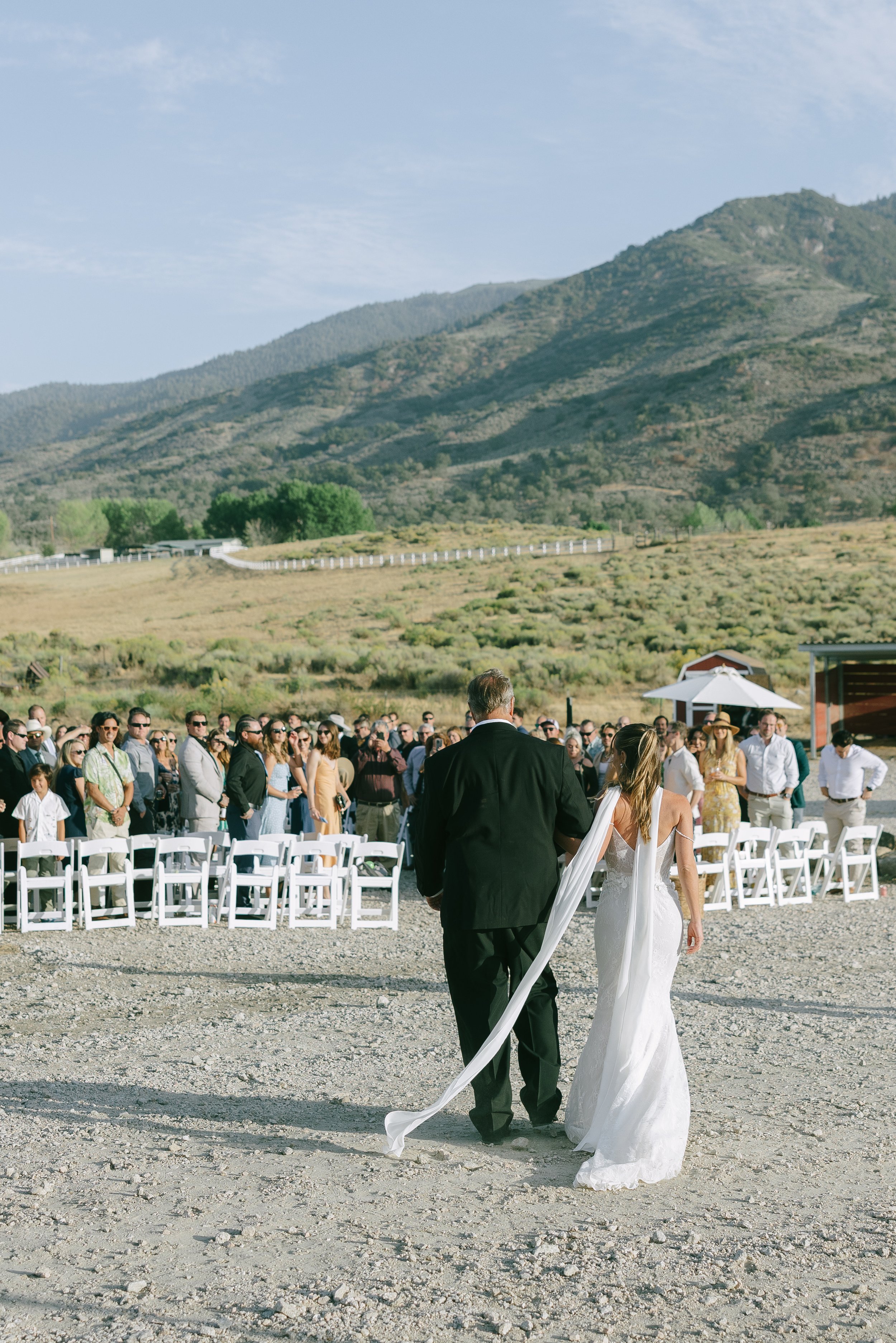 Bride and groom walking away from guests during an outdoor wedding ceremony in a scenic mountainous area.