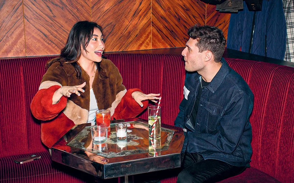 A woman and a man sitting in a booth at a restaurant, having drinks and engaging in conversation.