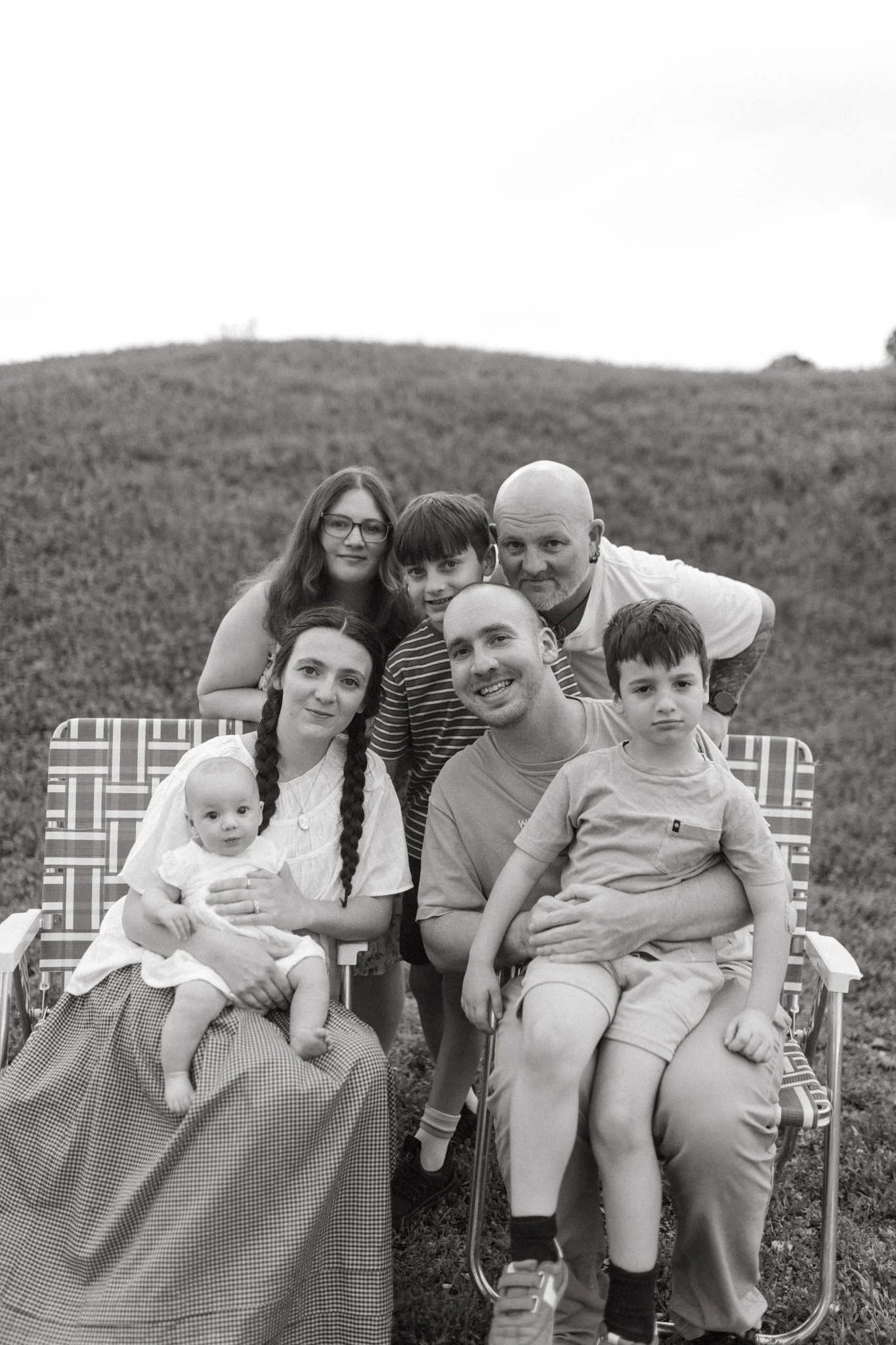 A black and white photo of a family outdoors, sitting on foldable chairs on a grassy hill.