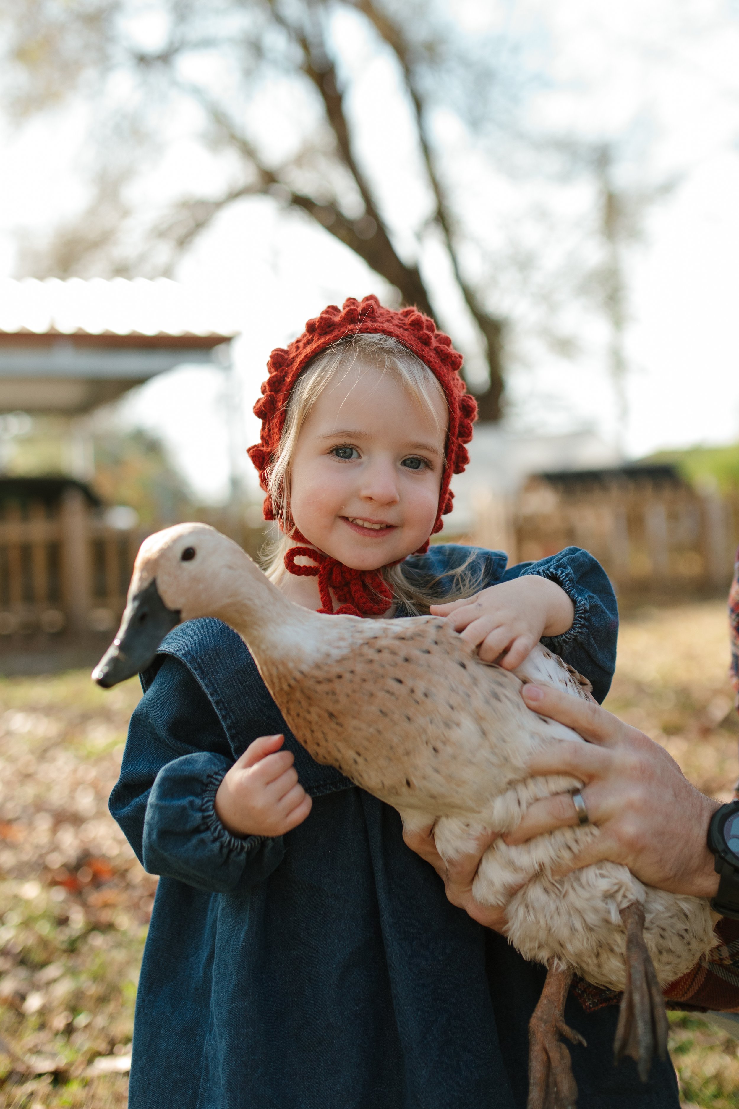 Smiling girl in a red knit hat holding a duck outdoors.