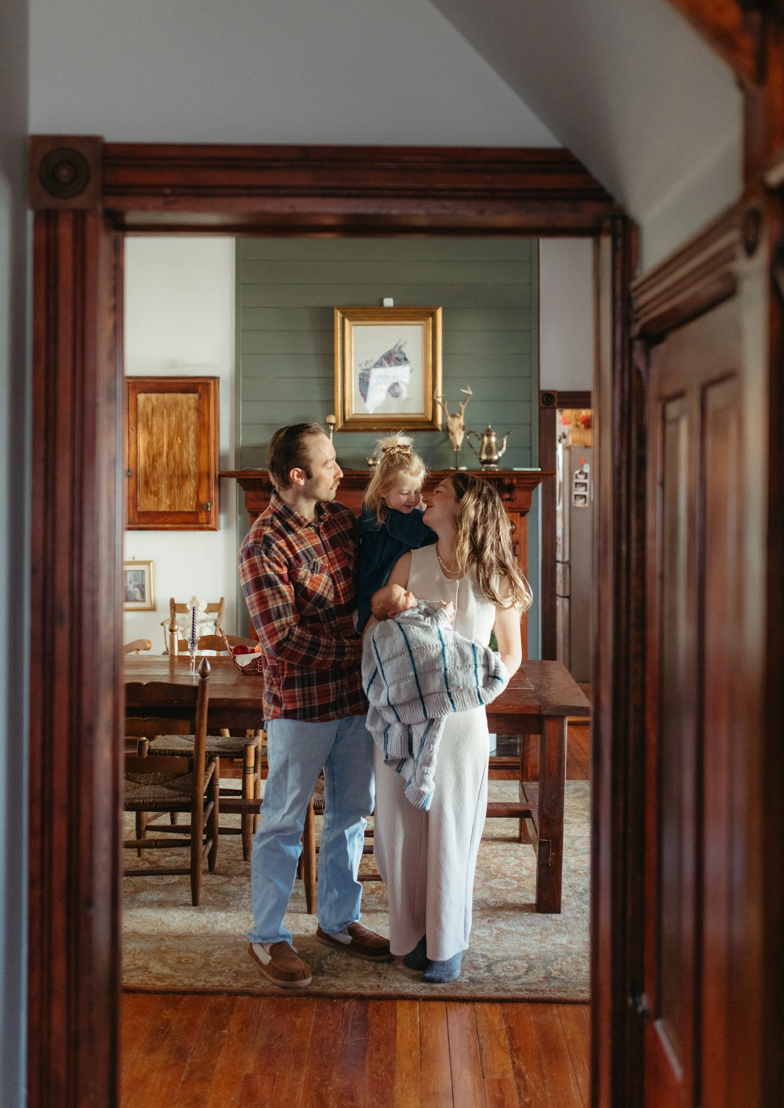 A family of four, including a man, woman, and two children, stands together in a cozy, vintage-style living room, sharing a joyful moment.