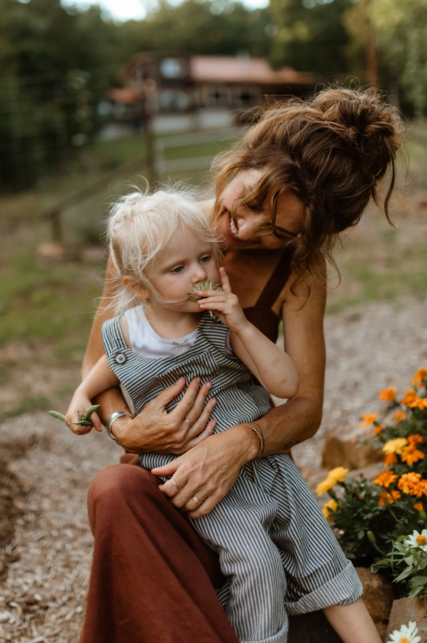 A woman and a young girl with blonde hair in an outdoor garden with orange flowers.