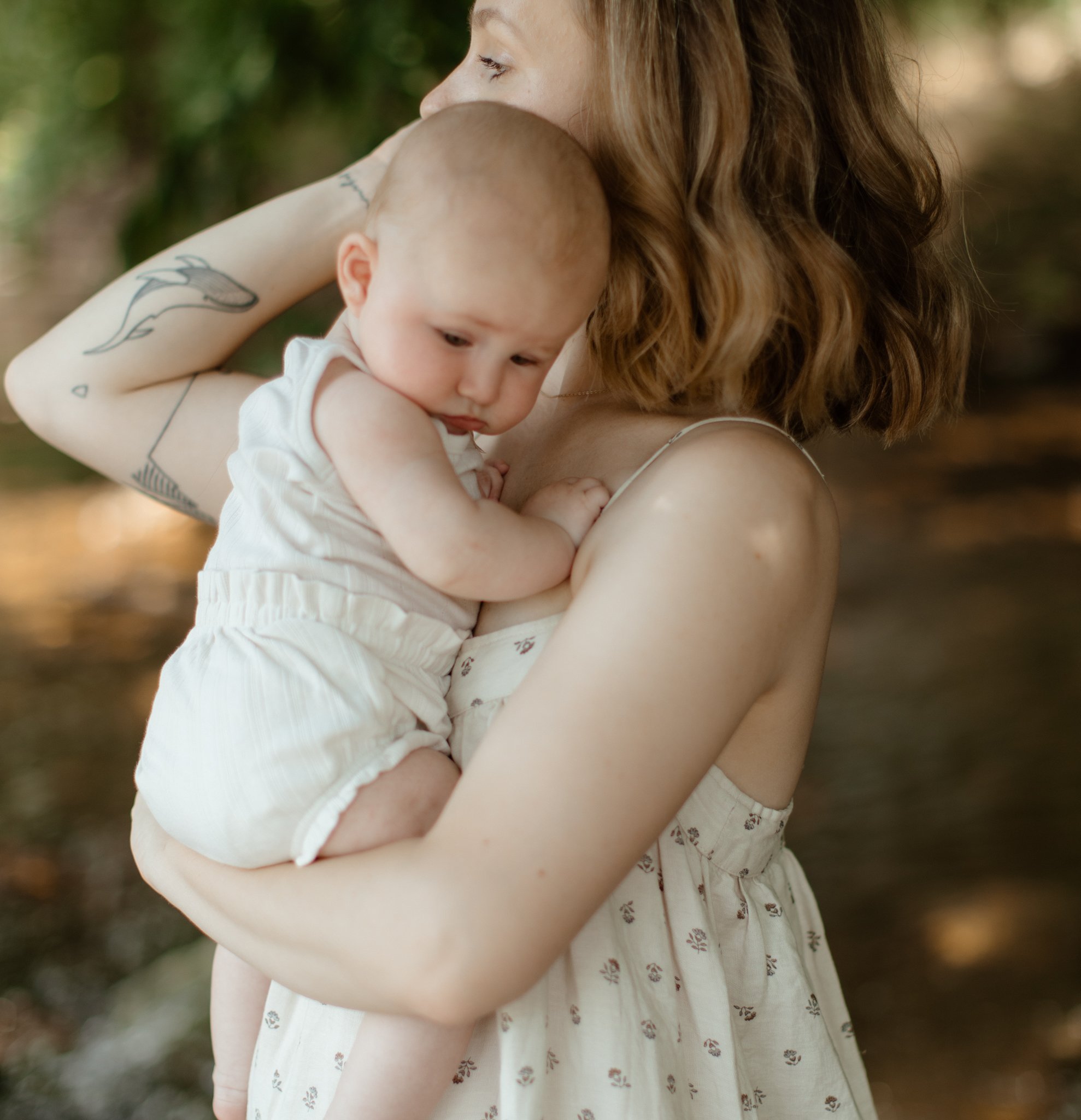 A woman with red hair holding a young baby against her shoulder outdoors.