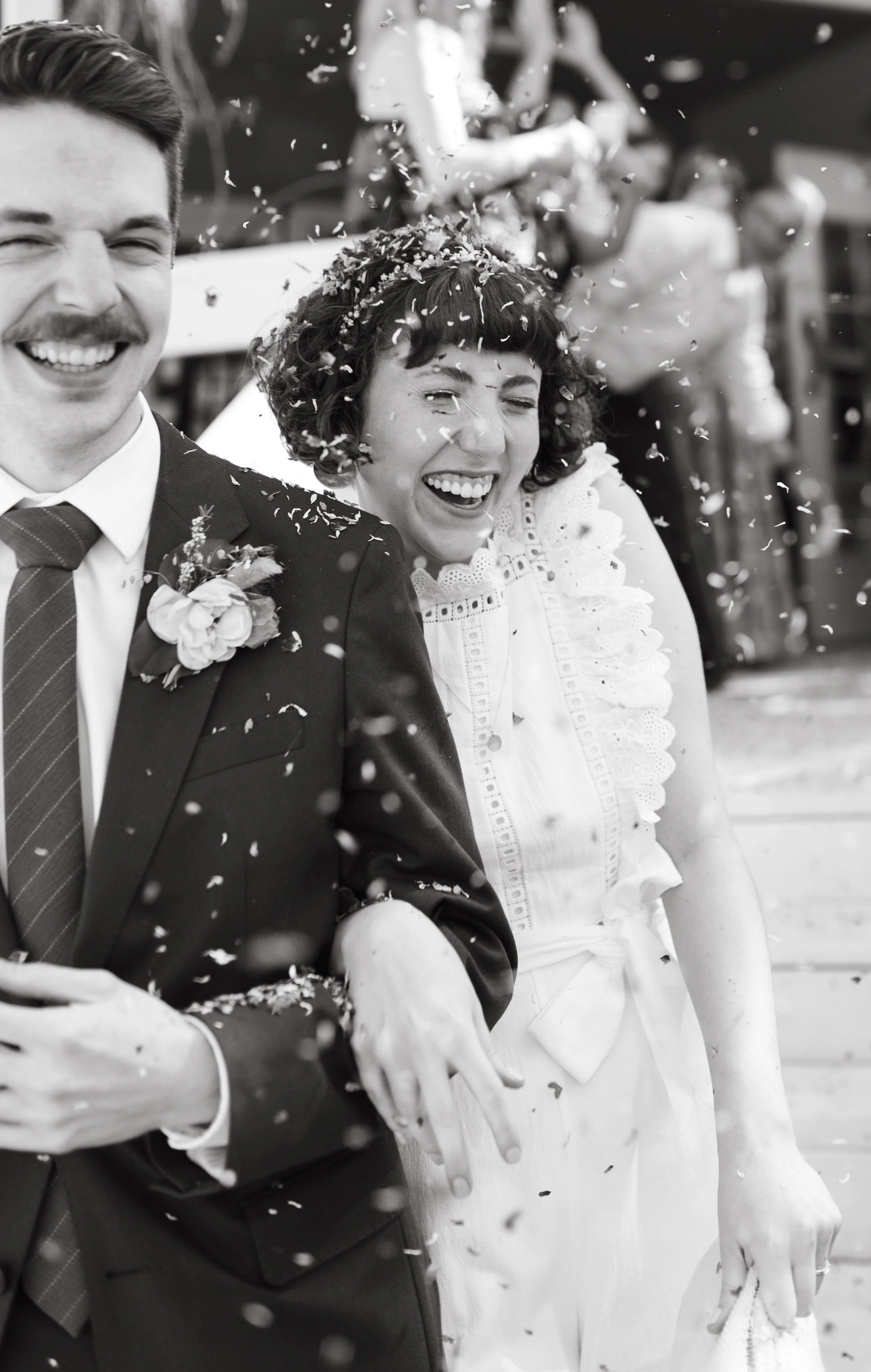 A black-and-white photo of a joyful bride and groom celebrating their wedding, with confetti falling around them.
