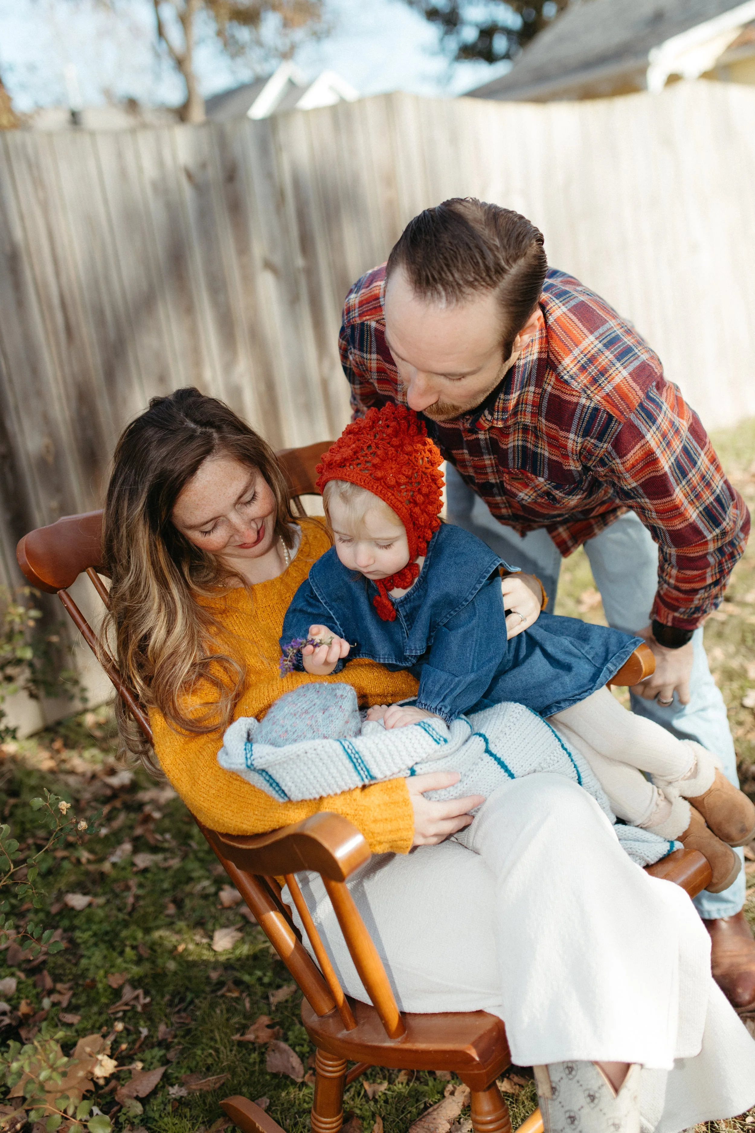 Family outdoors with mother, father, and two young children, one in a baby rocker, enjoying fall foliage.