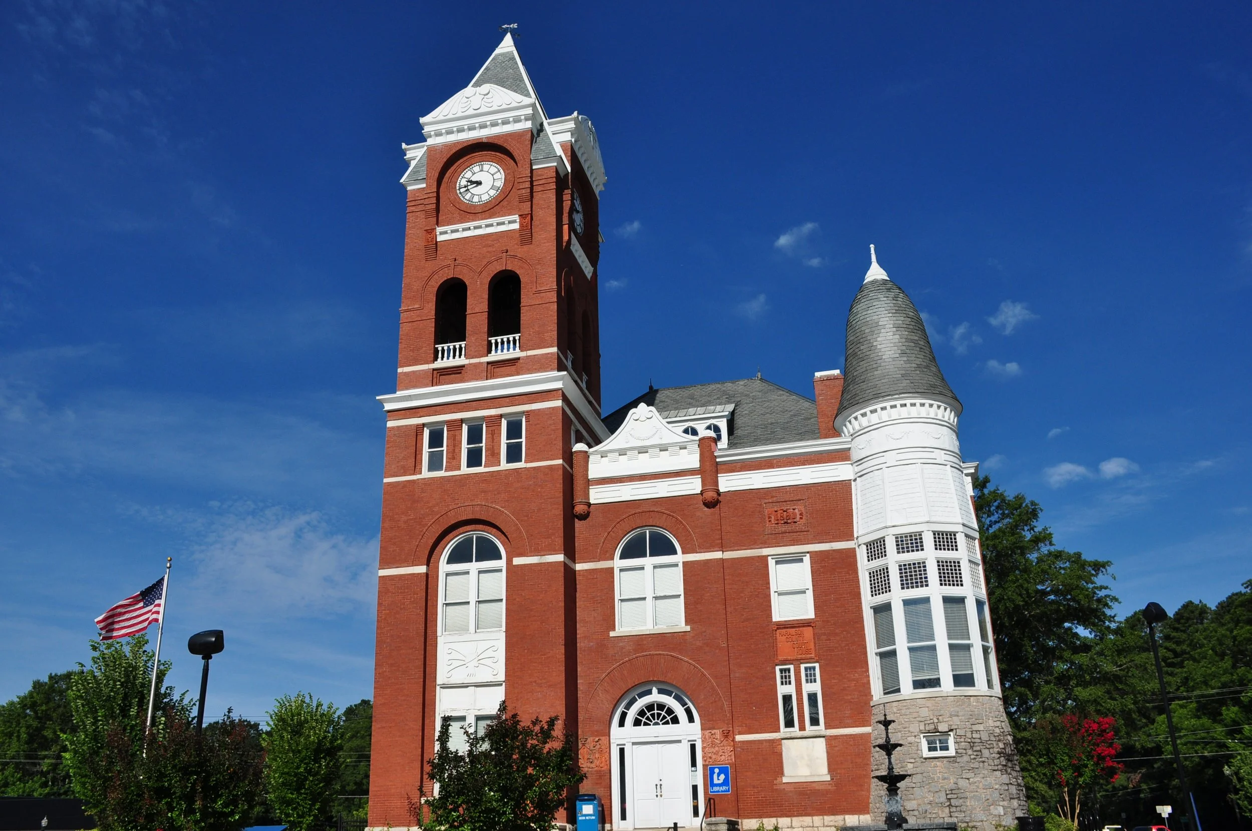 A historic red brick courthouse with a tall clock tower and a turret, set against a blue sky.