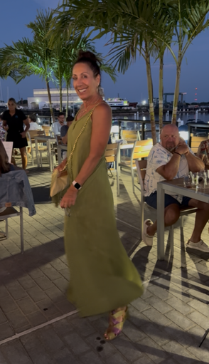 woman smiling in green dress in front of palm trees and the water on a restaurant deck
