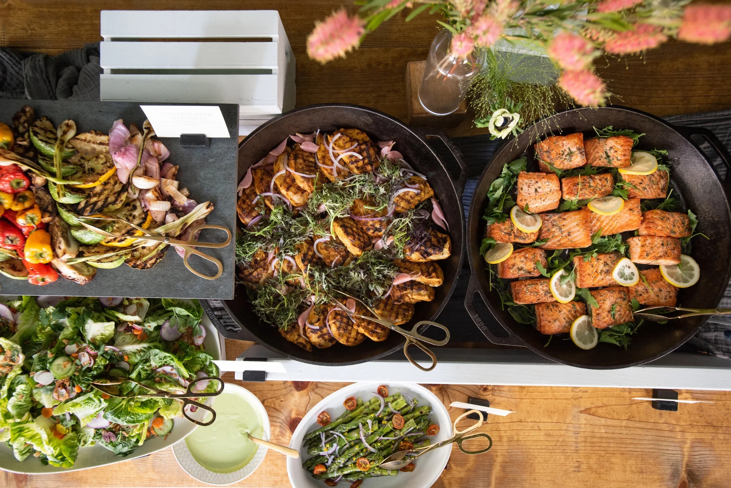 A buffet of grilled vegetables, salads, and salmon fillets garnished with lemon slices.