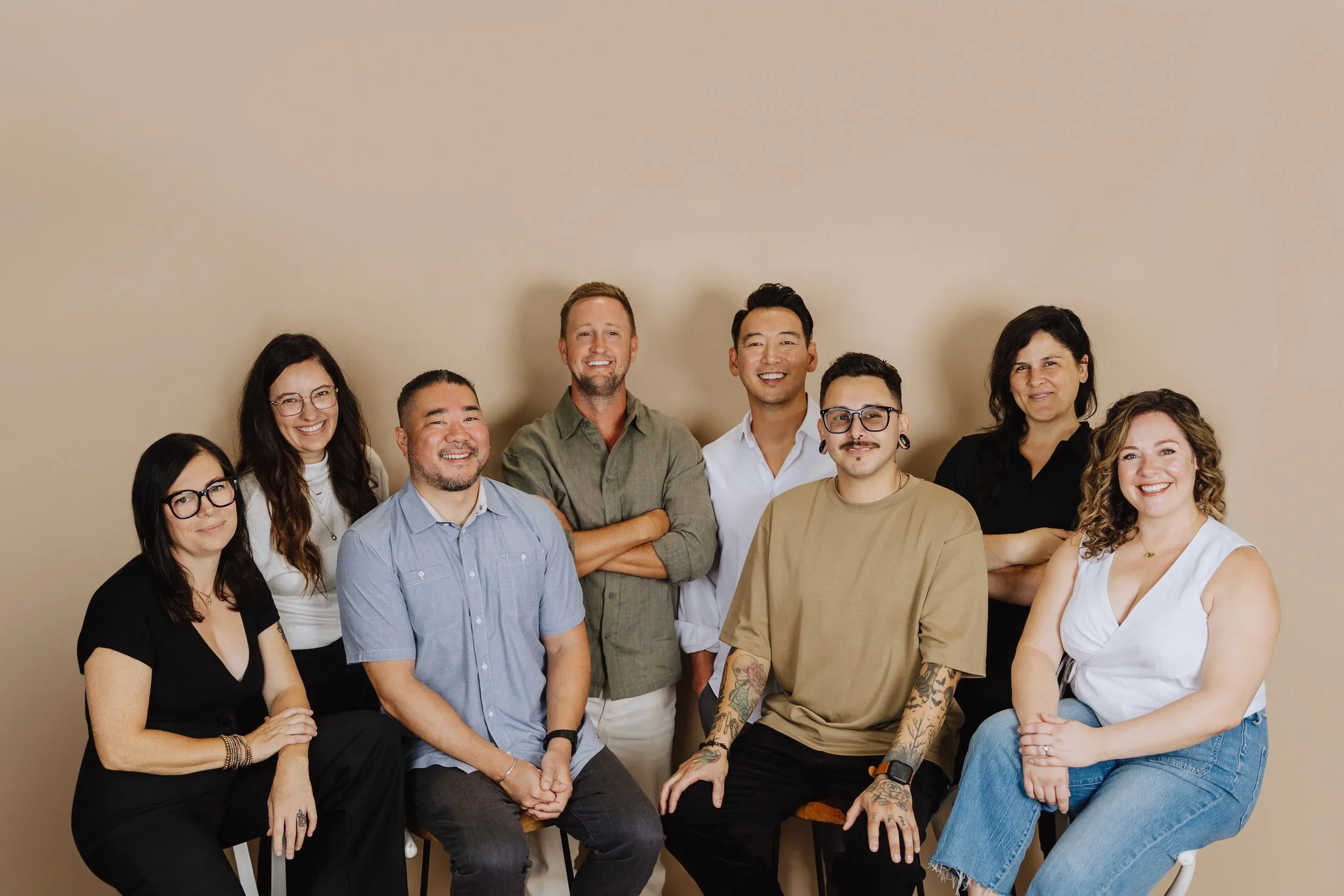 Group of nine diverse adults smiling, seated and standing against a beige background.