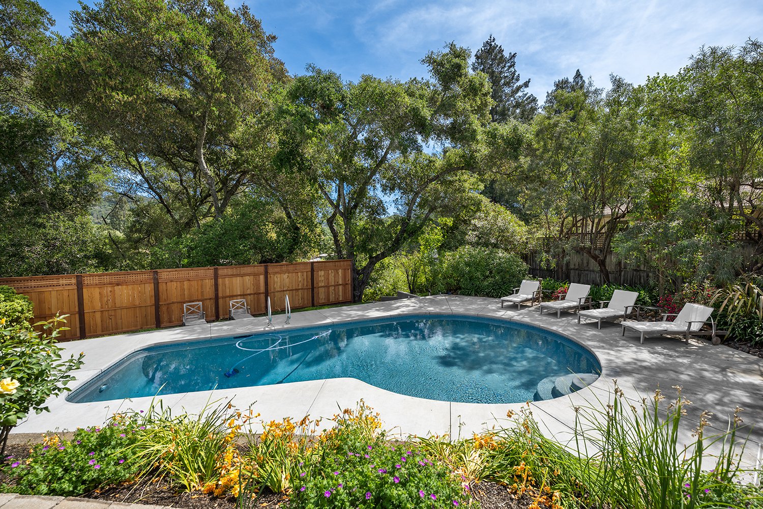 A modern white house with a divided front porch, three trees in the front yard, and a paved driveway leading to a two-car garage, under a clear blue sky.