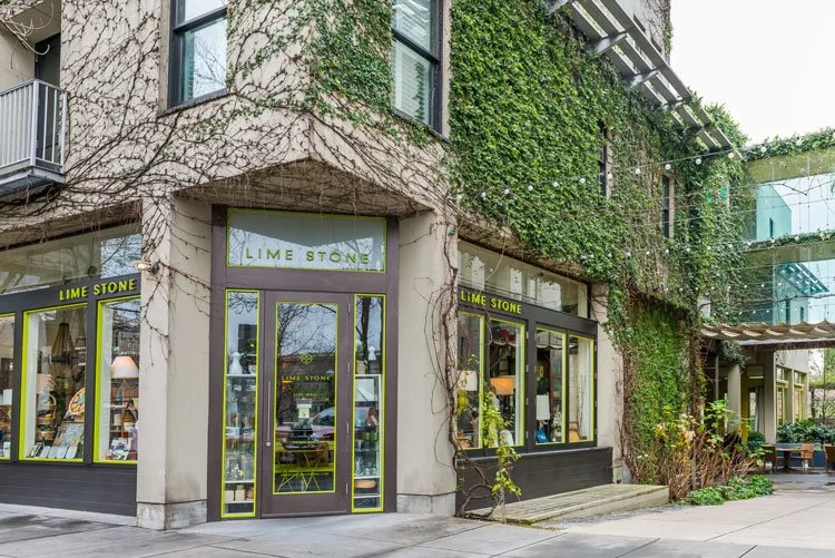 Exterior of a store called Lime Stone with large glass windows and a door, surrounded by green ivy vines and string lights outside.