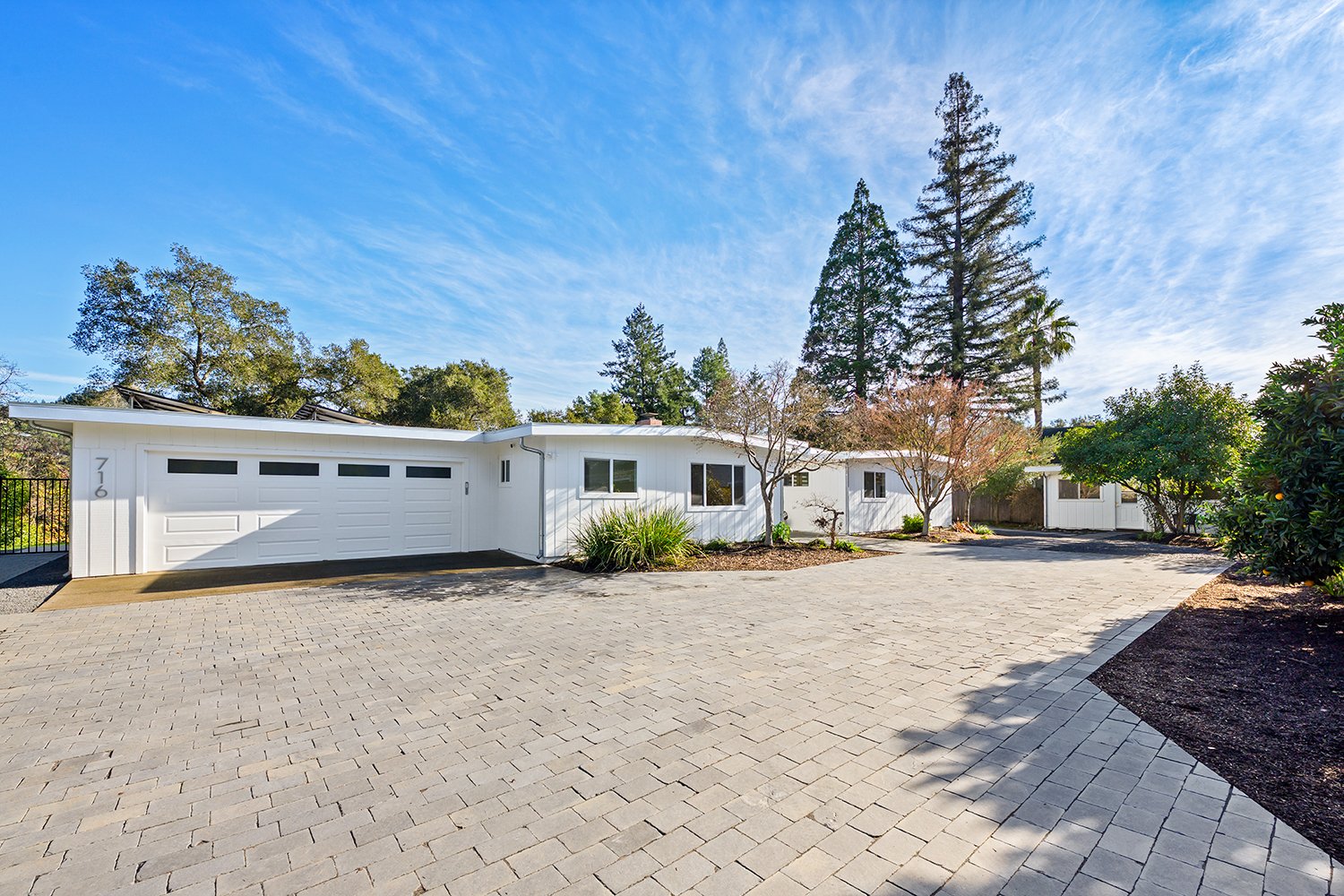 White modern house with a large driveway, surrounded by trees and a clear blue sky.
