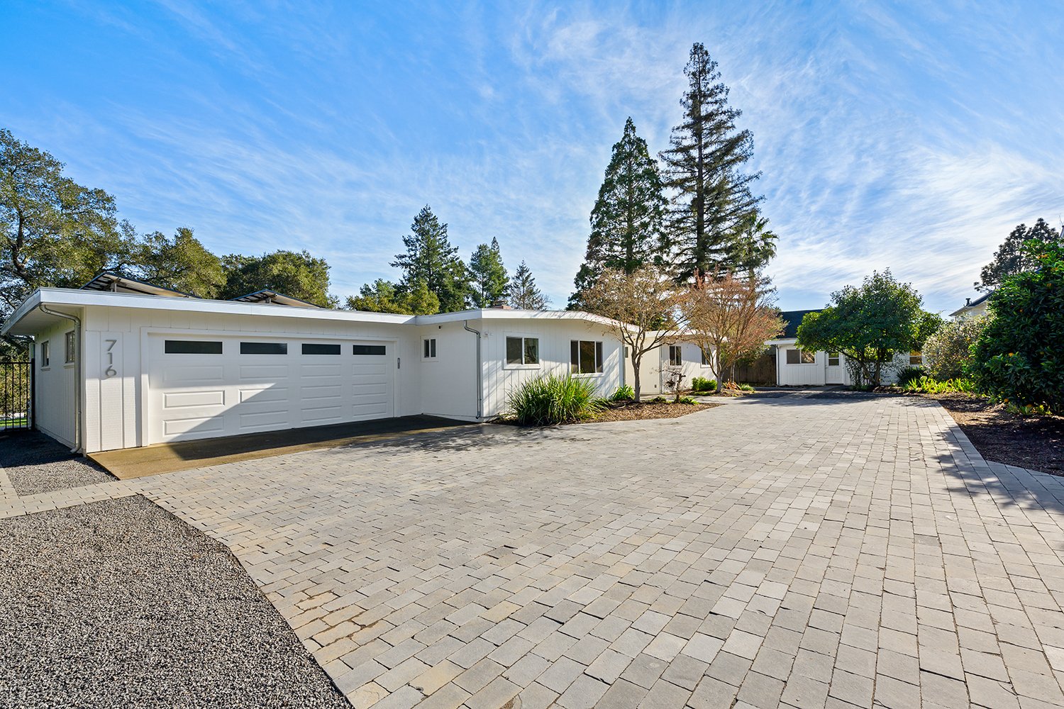 Frontyard view of a modern house with white exterior, driveway, garage, trees, and clear sky.