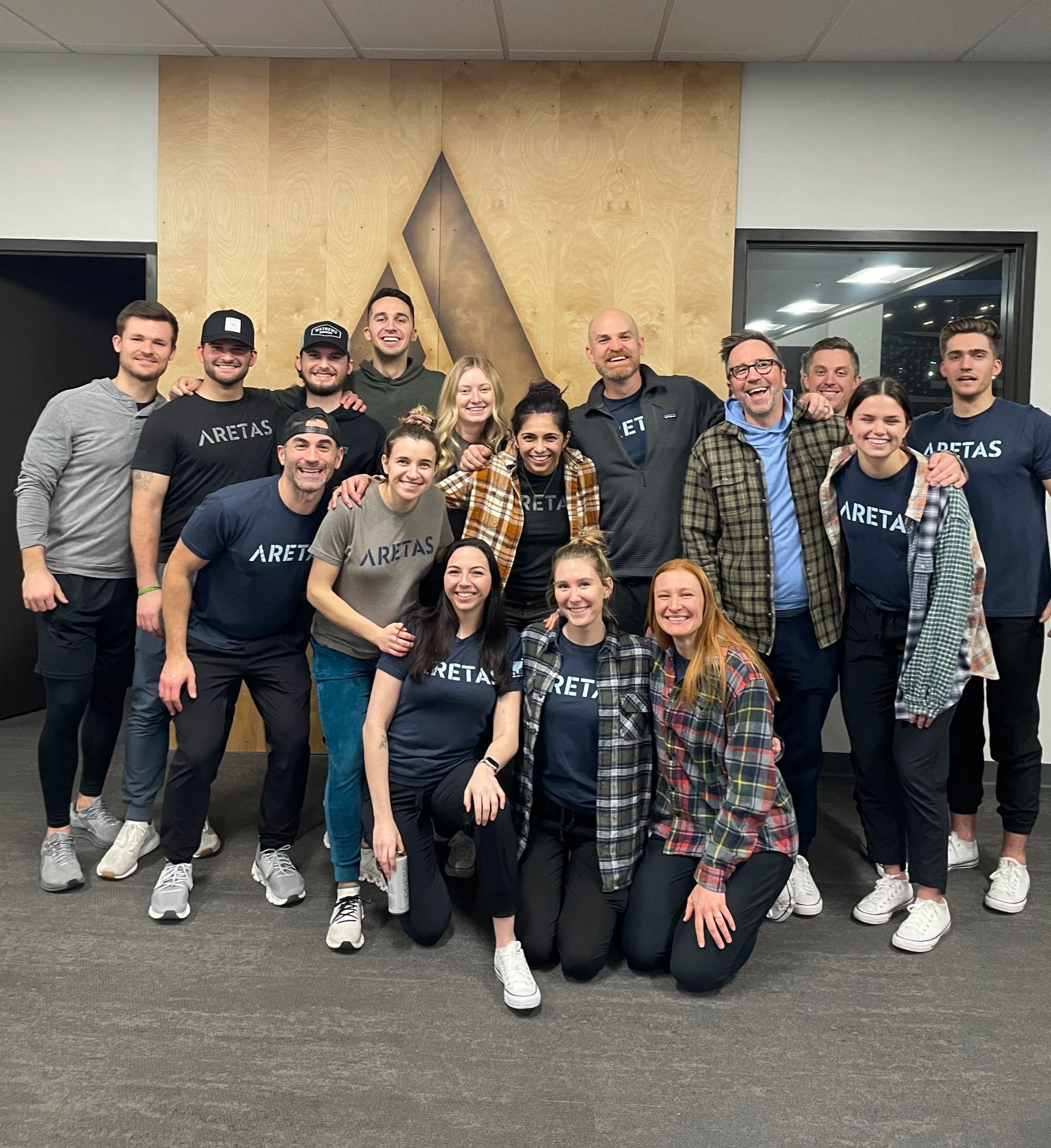 Staff photo of 16 people both male and female standing together and smiling all wearing "aretas" t-shirts
