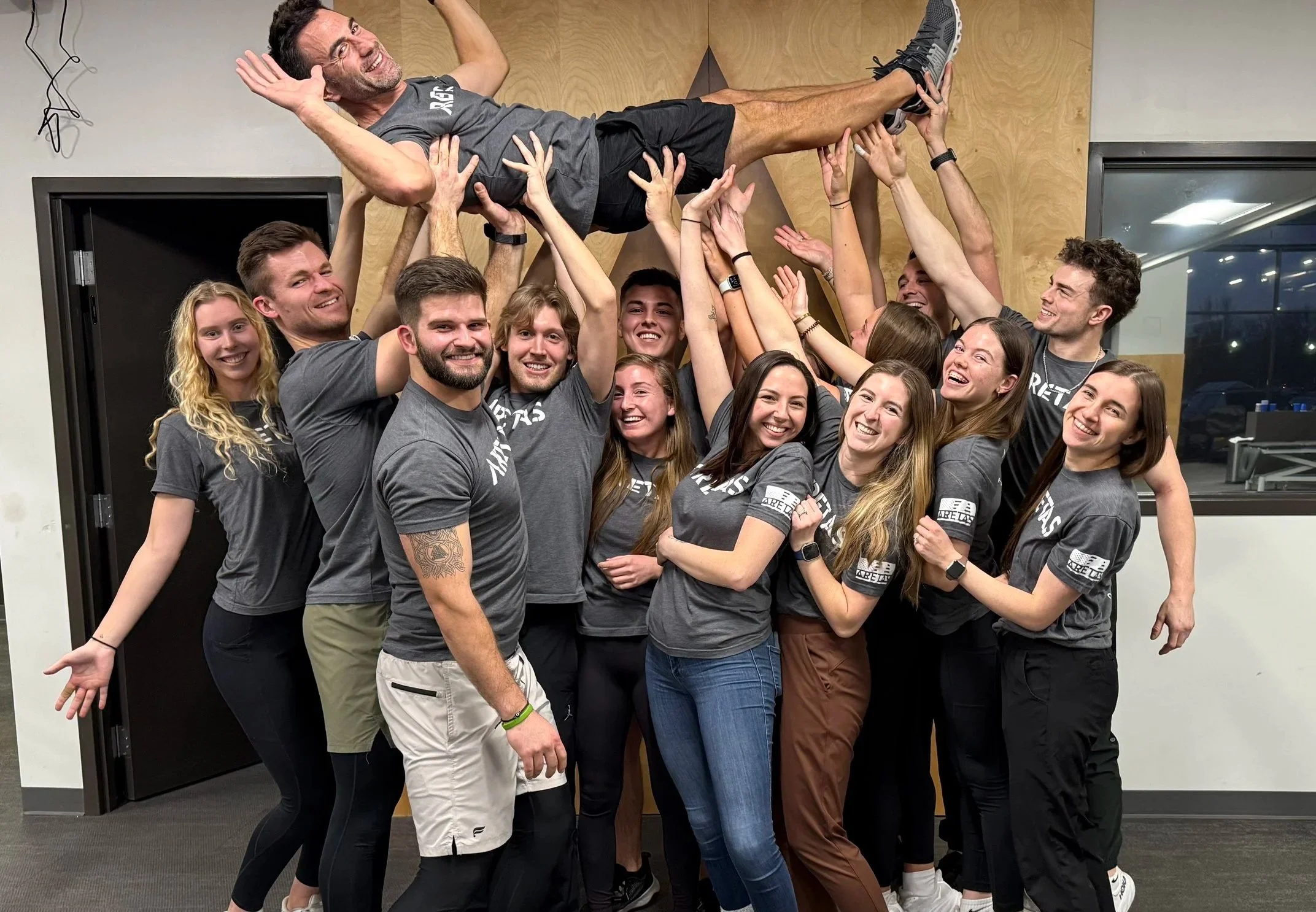 Aretas staff, wearing gray Aretas shirts, hold Kevin, the Aretas Physical Therapy Hales Corners owner, overhead while he crowd surfs
