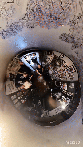 A distorted, circular view of people in a room with framed pictures on the walls, used for a 360-degree photo or selfie.