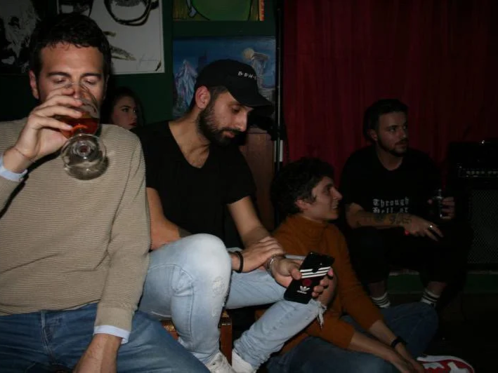 Group of young adults sitting in a bar or club, some drinking and looking at their phones.