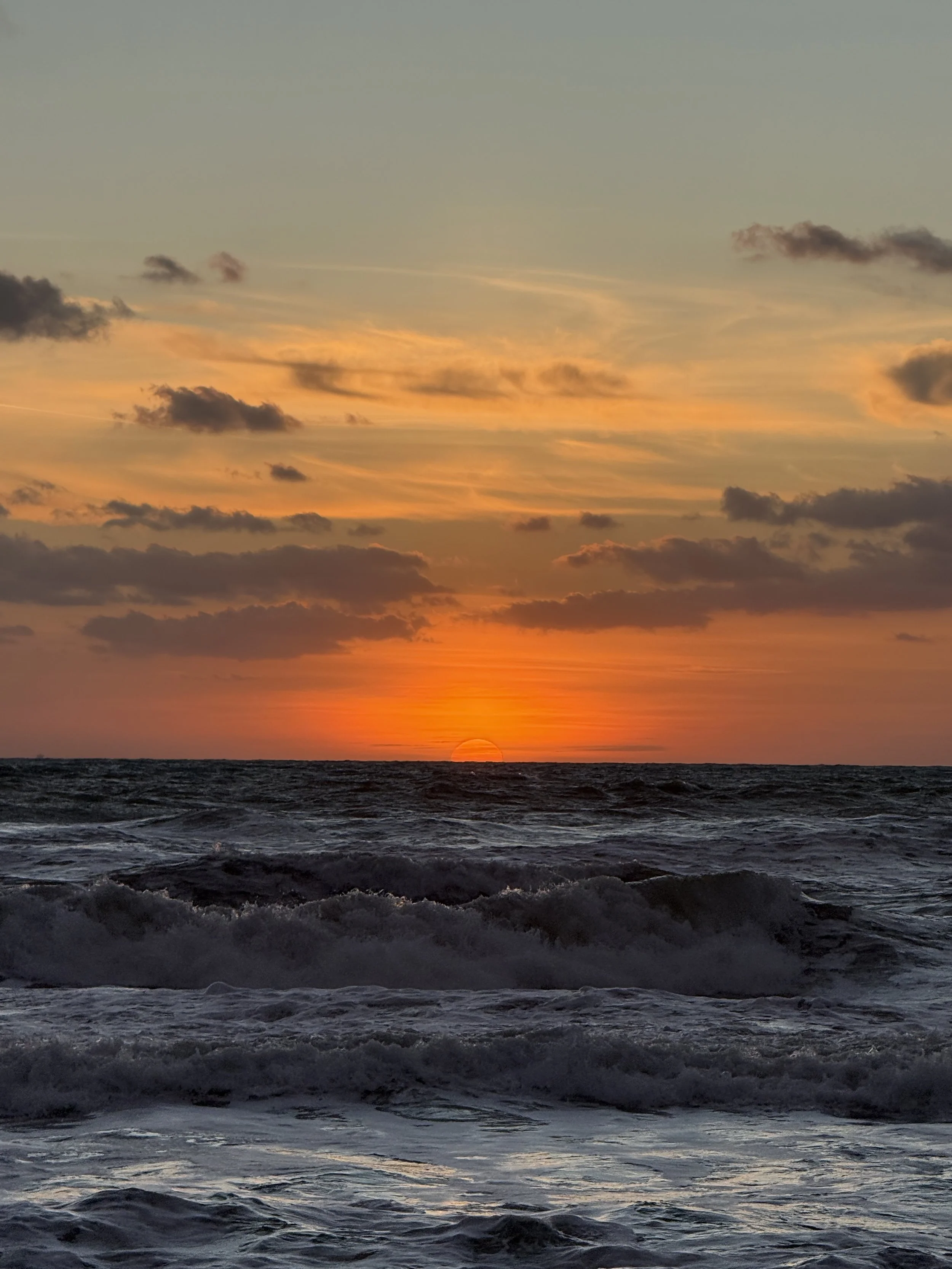 Sunset over the ocean with waves and clouds in the sky.