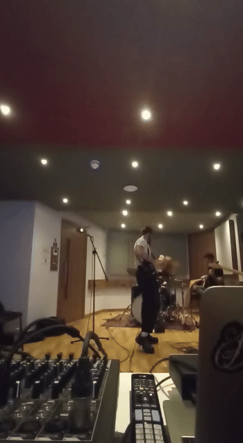 A person playing the drums on stage in a recording studio with musical equipment visible in the foreground."