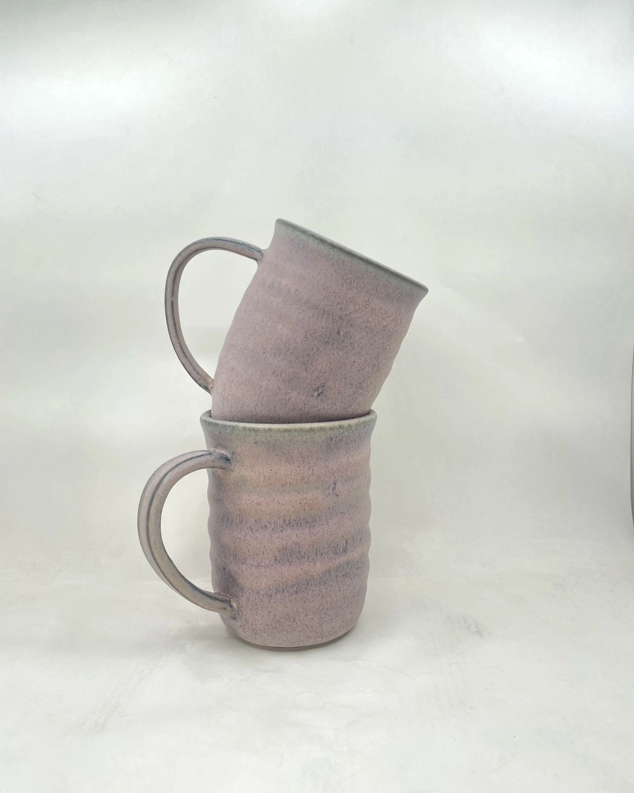 Two stacked ceramic mugs with a textured, pastel-colored glaze against a plain white background.
