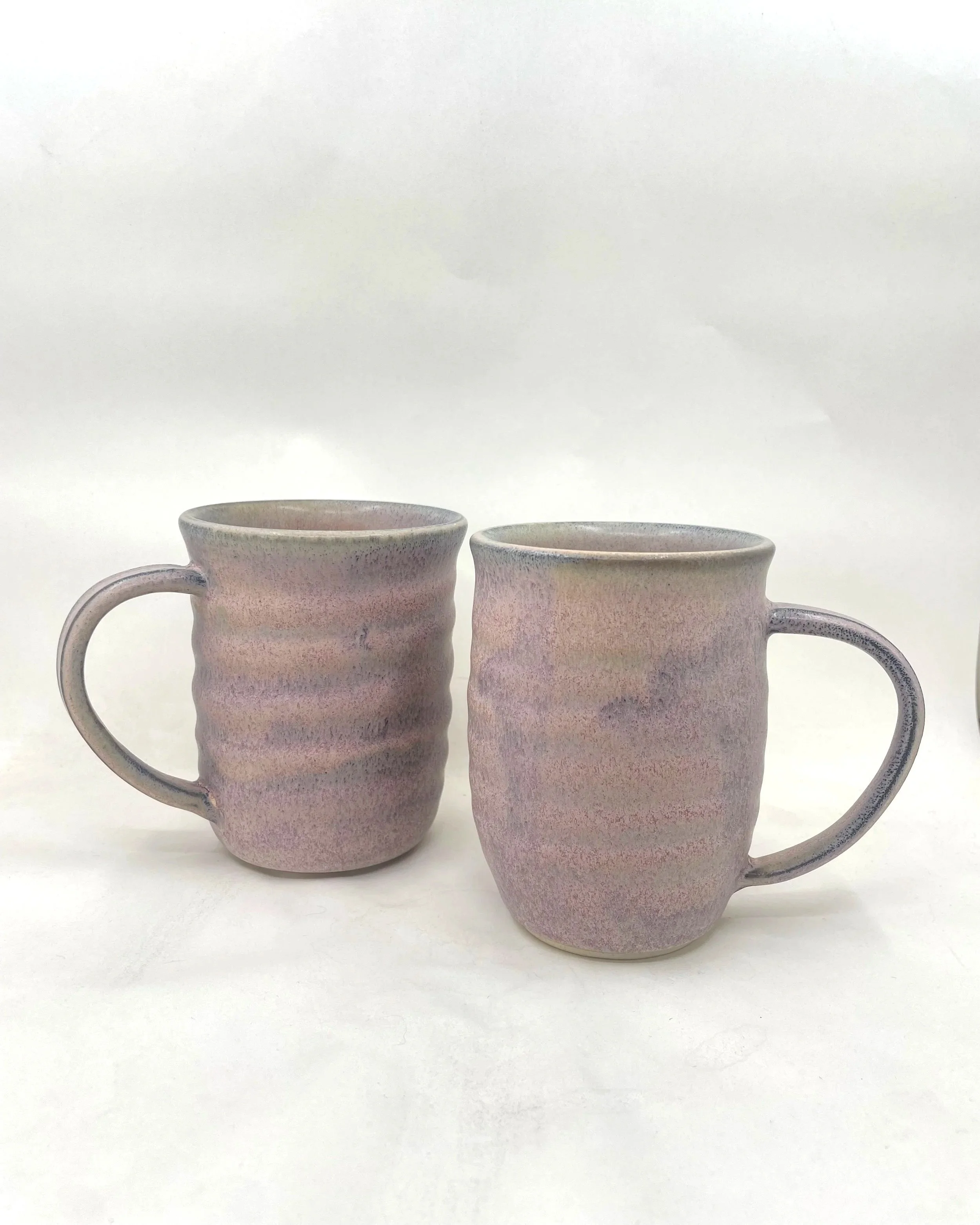 Two ceramic mugs with wavy textures and pastel, mottled glaze, positioned on a white surface against a white background.
