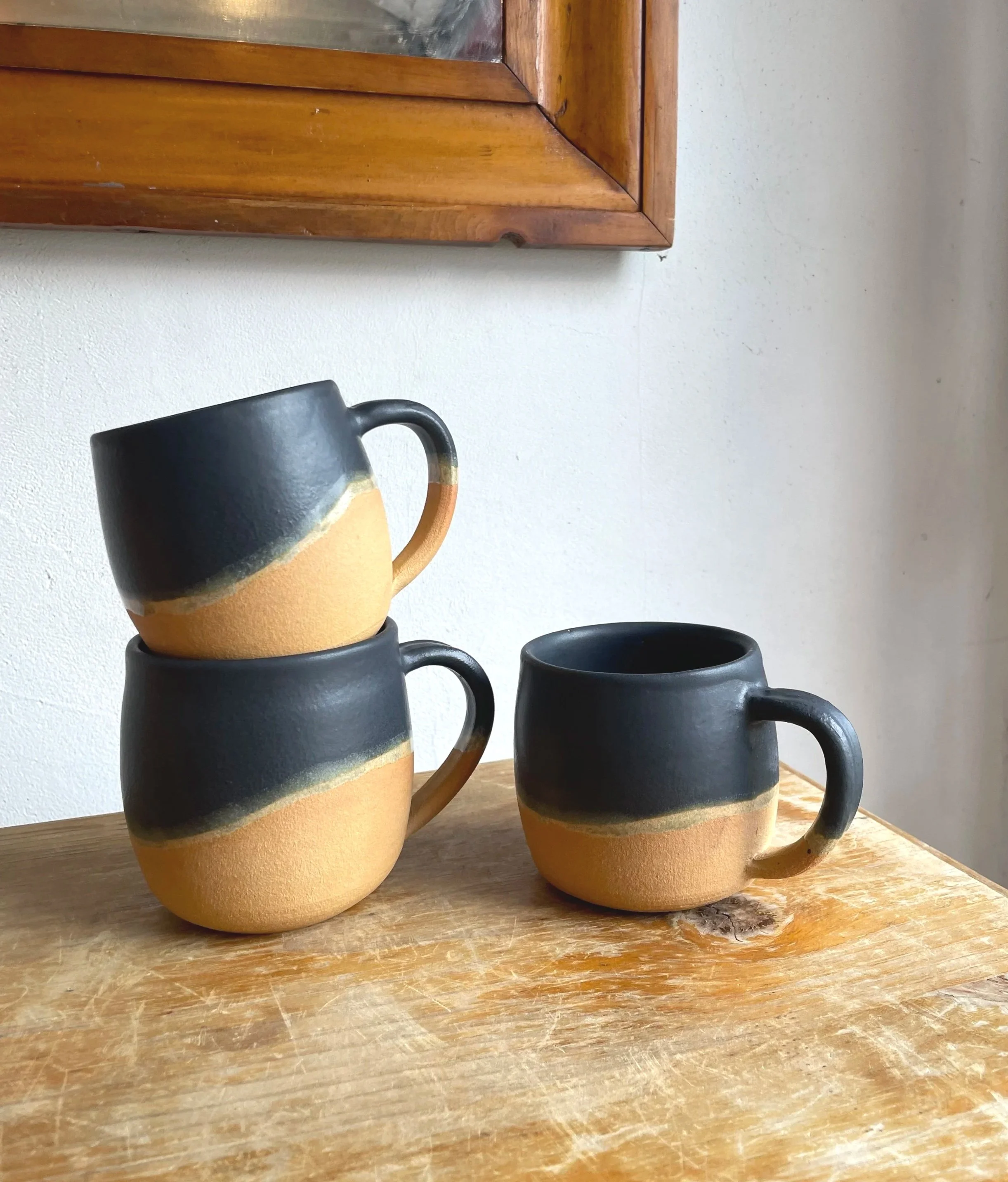 Coffee mugs hand thrown with a warm orange clay, and glazed with a black satin glaze, and a band of golden honey