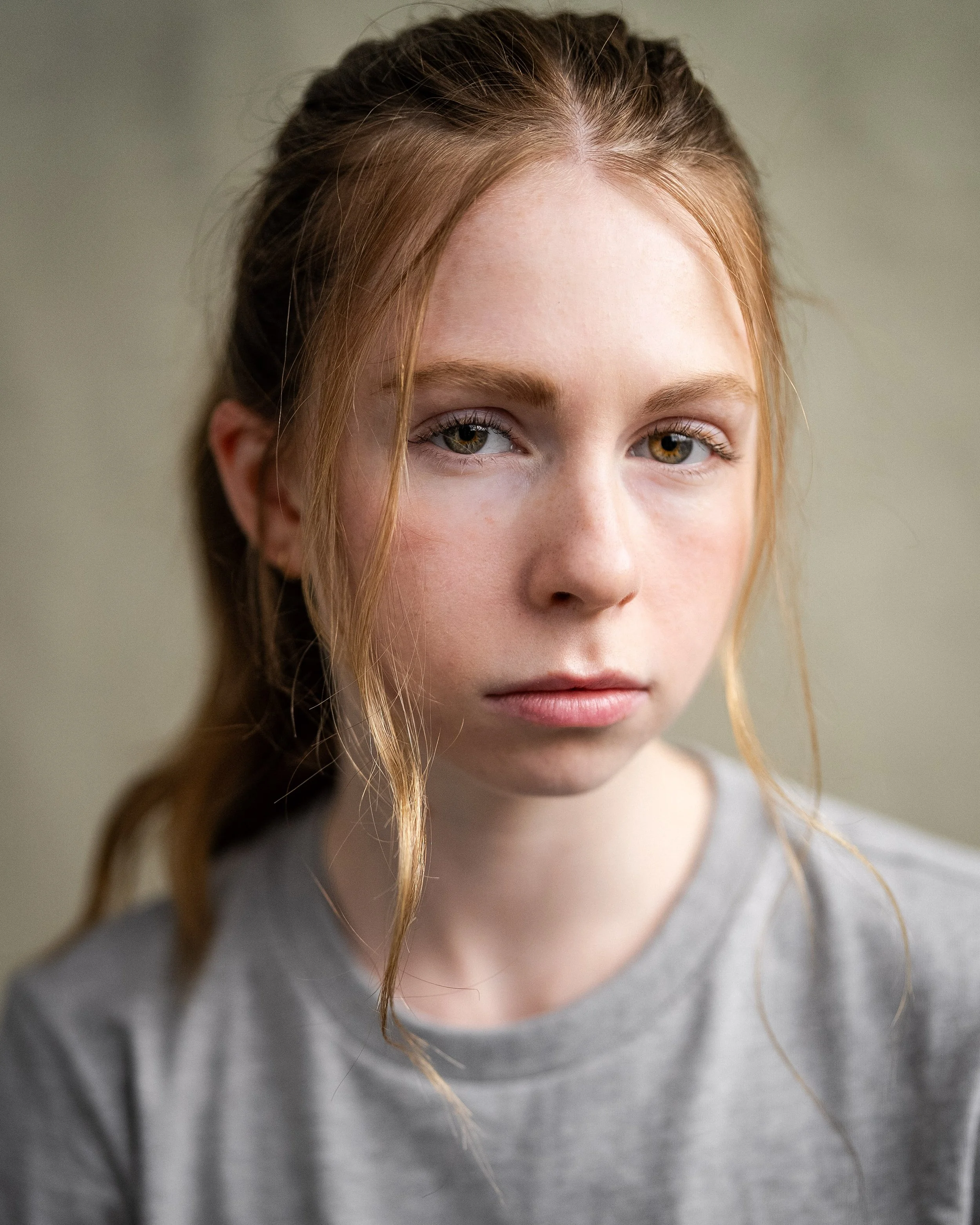 Close-up of a young woman with red hair and green eyes wearing a gray shirt against a plain background. Stranger Things.