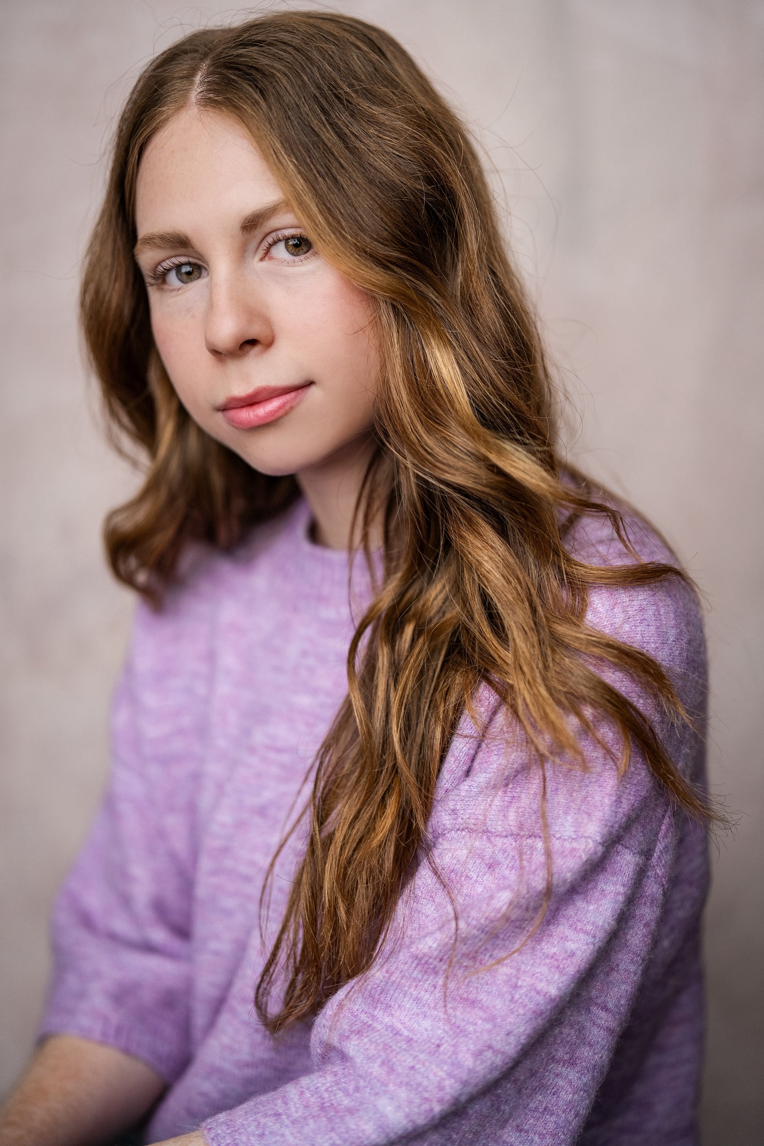 Close-up portrait of a young woman with red hair, wearing a light purple sweater, looking at the camera with a neutral expression. Pretty girl. 