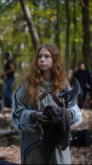 Young woman in medieval costume holding an axe in a forest setting. Merida from Brave.