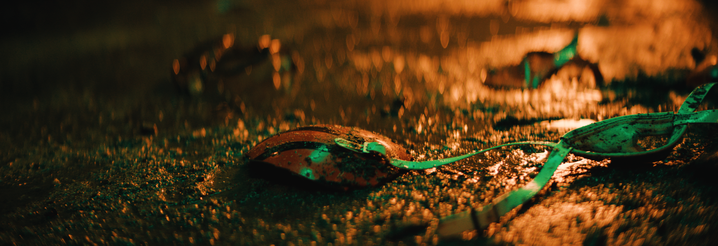 Close-up of broken swimming goggles on wet surface with blurred, warm lighting in the background. Cleveland Browns. Sports director of photography camera operator. Arri Alexa 35 anamorphics.