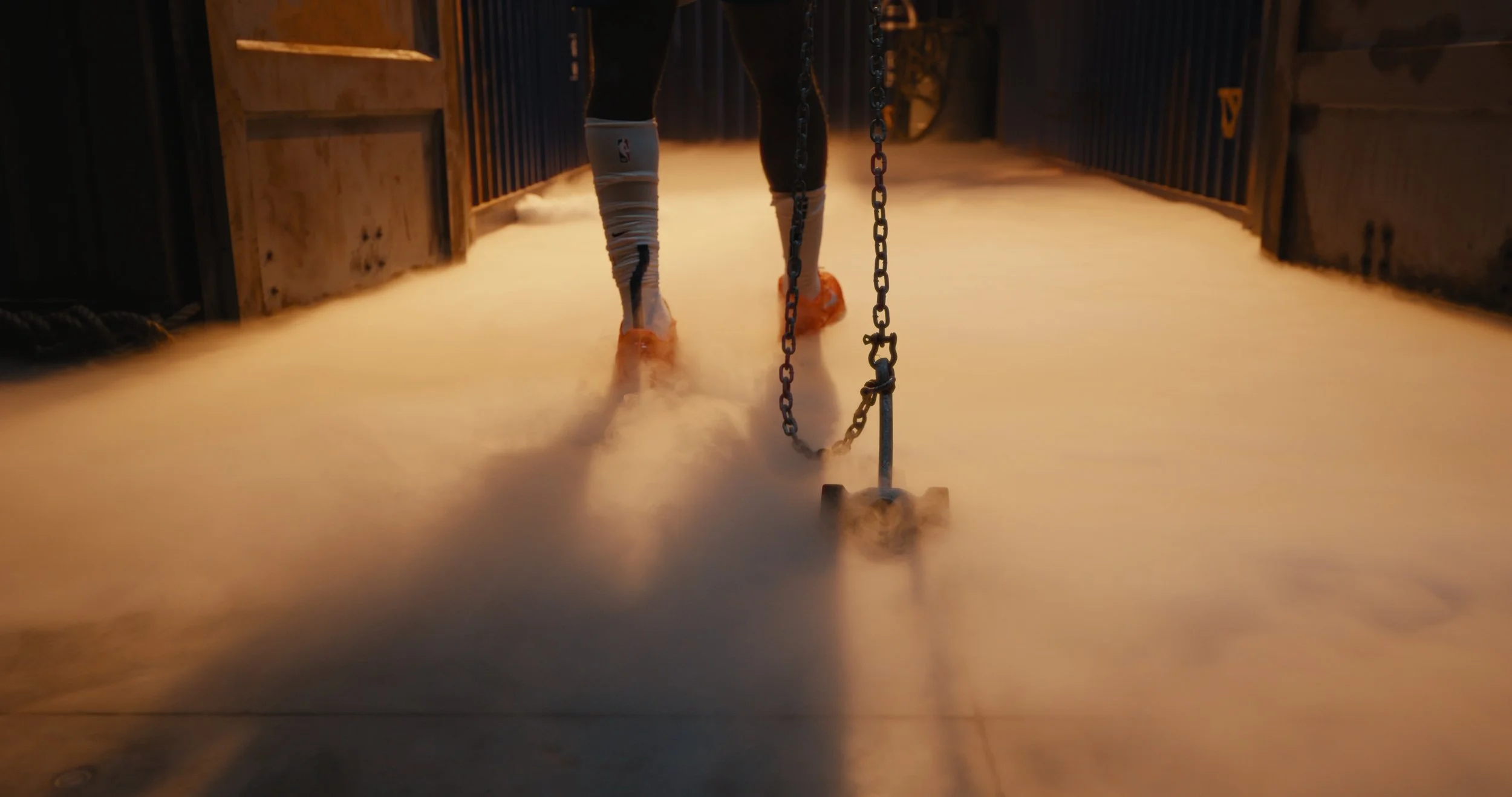 A person walking on what appears to be a foggy or misty surface, possibly snow or a foggy scene, with orange shoes and legs in black pants, holding a chain.