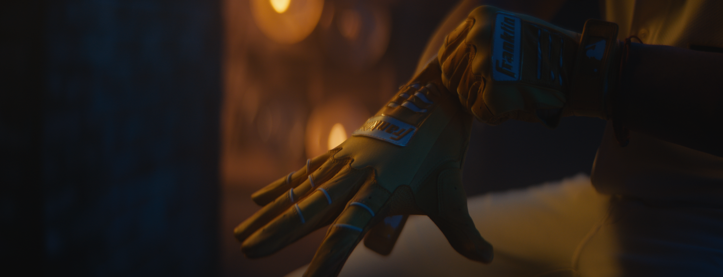 Close-up of a motorcycle racing glove on a person's hand, resting on a surface, with blurred warm lights in the background.