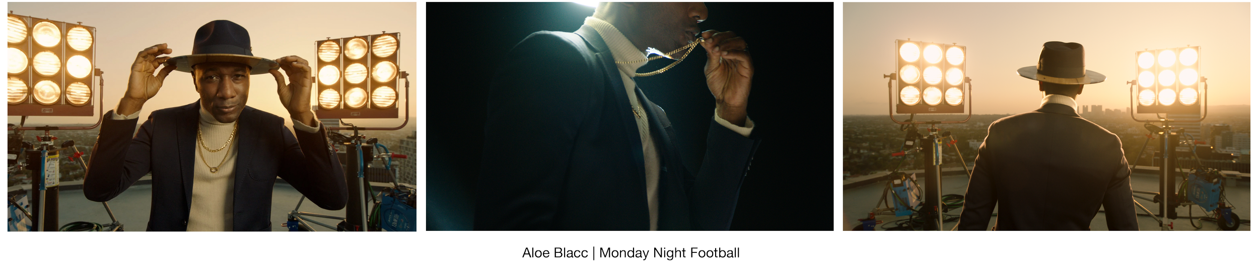 A man in a suit with a hat and gold chains poses in front of cityscape at sunrise with studio lights in the background, then turns away, holding a chain, during a photo shoot.