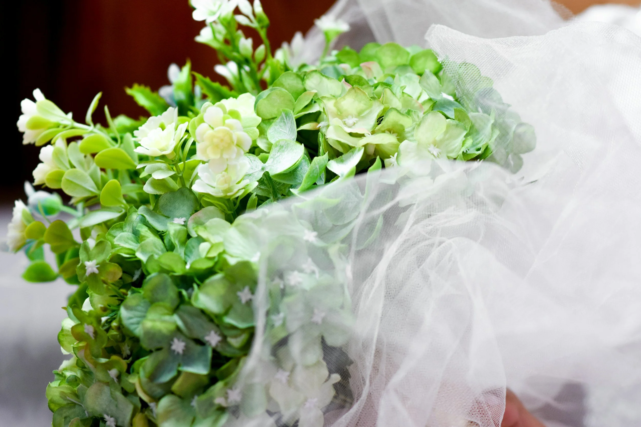 A bouquet of green and white hydrangea flowers wrapped in sheer white fabric.
