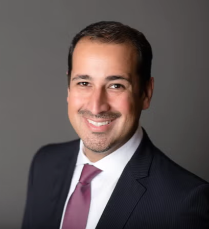 Portrait of a smiling man in a suit with a gray background.