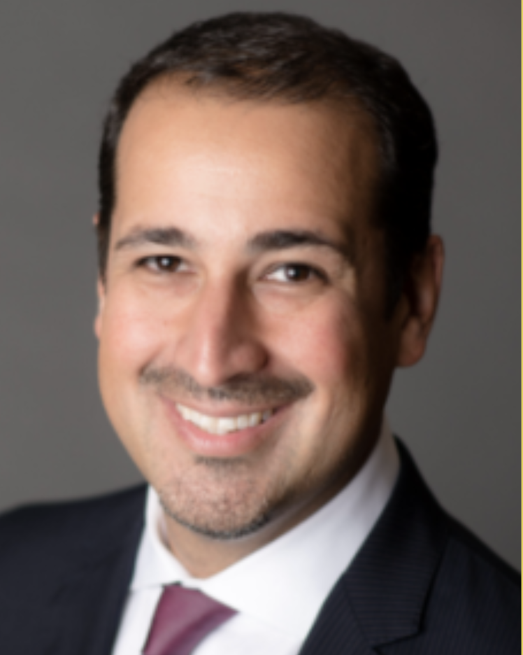 Portrait of a smiling man in a suit with a gray background.