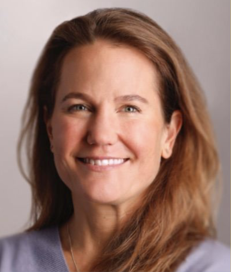 A woman with shoulder-length reddish-brown hair smiling at the camera against a gray background.