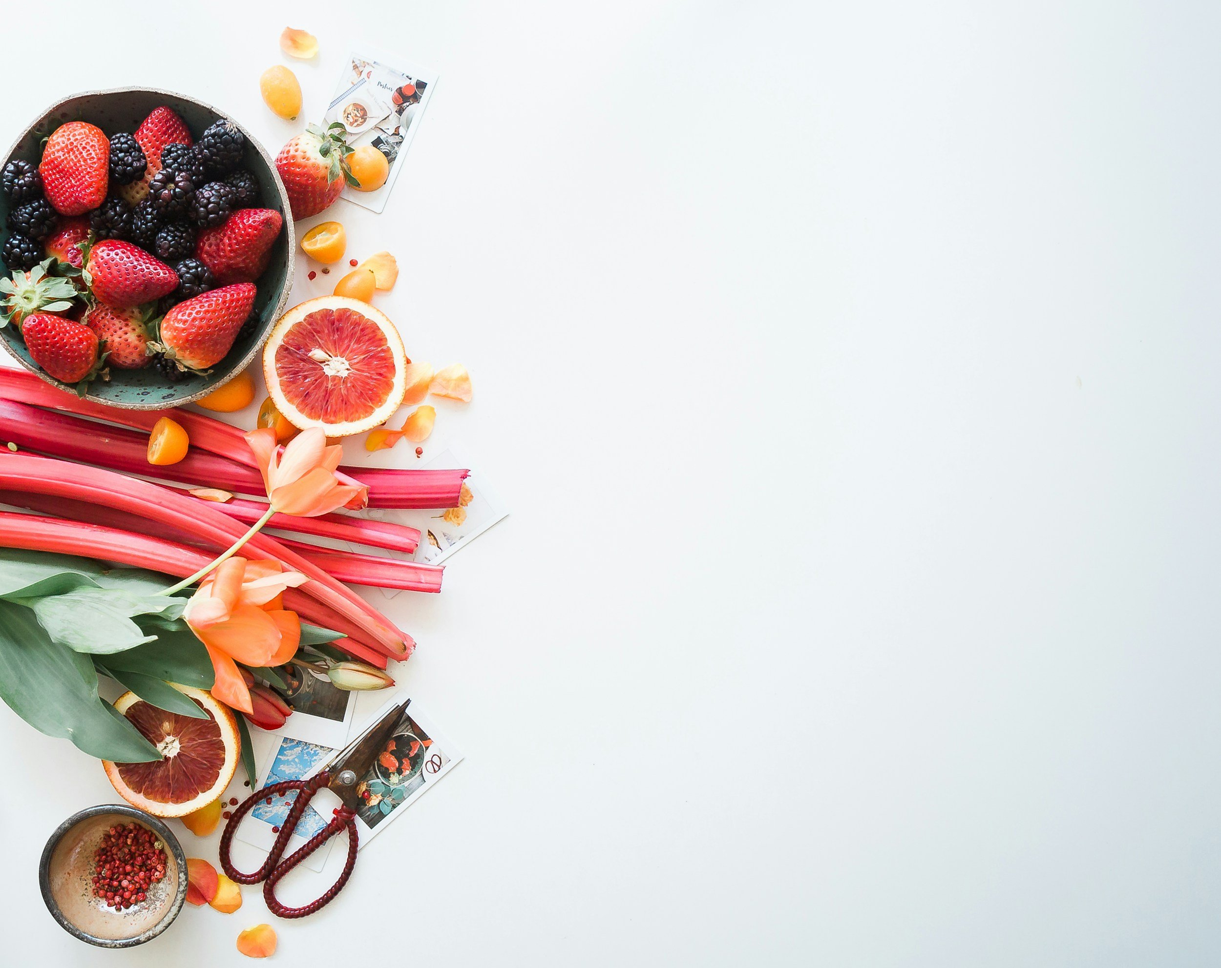 A flat lay of assorted fresh berries, rhubarb, flowers, and gardening tools on a white background. Longevity. Healthy. better health.