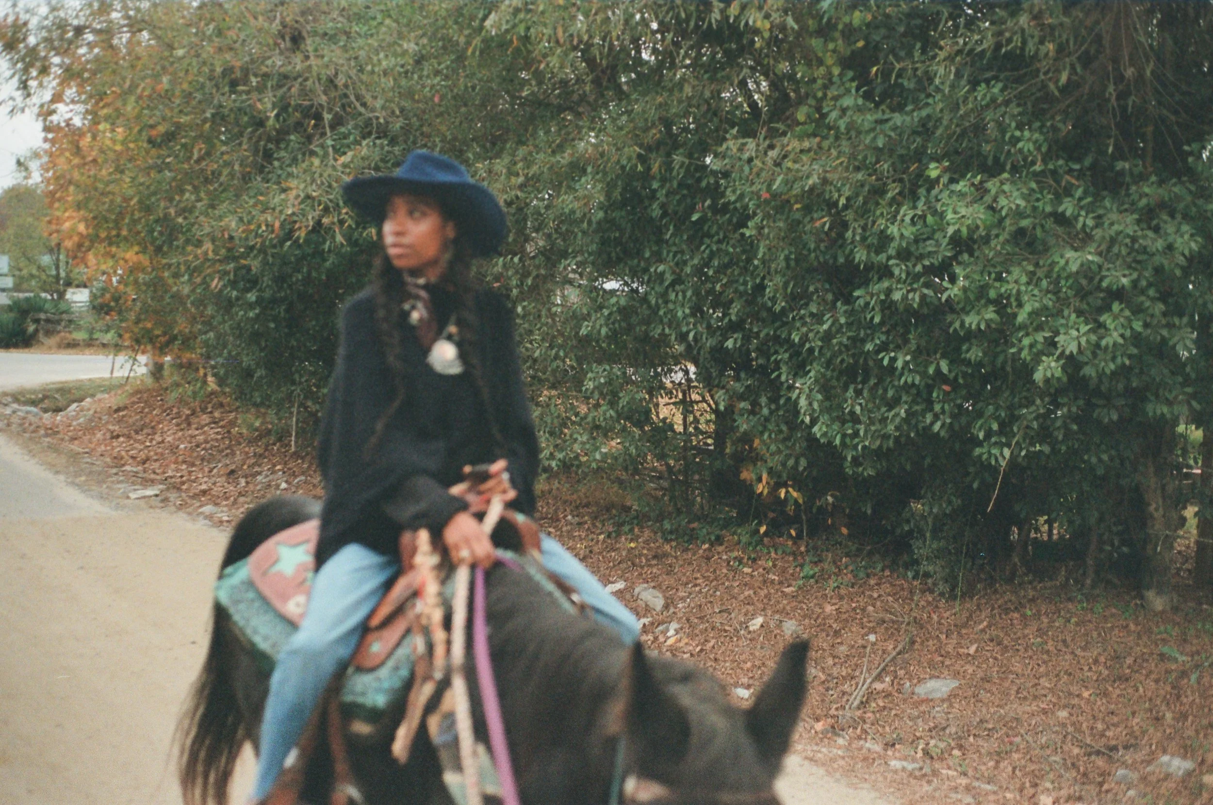 A woman riding a horse along a dirt path with trees and foliage in the background.