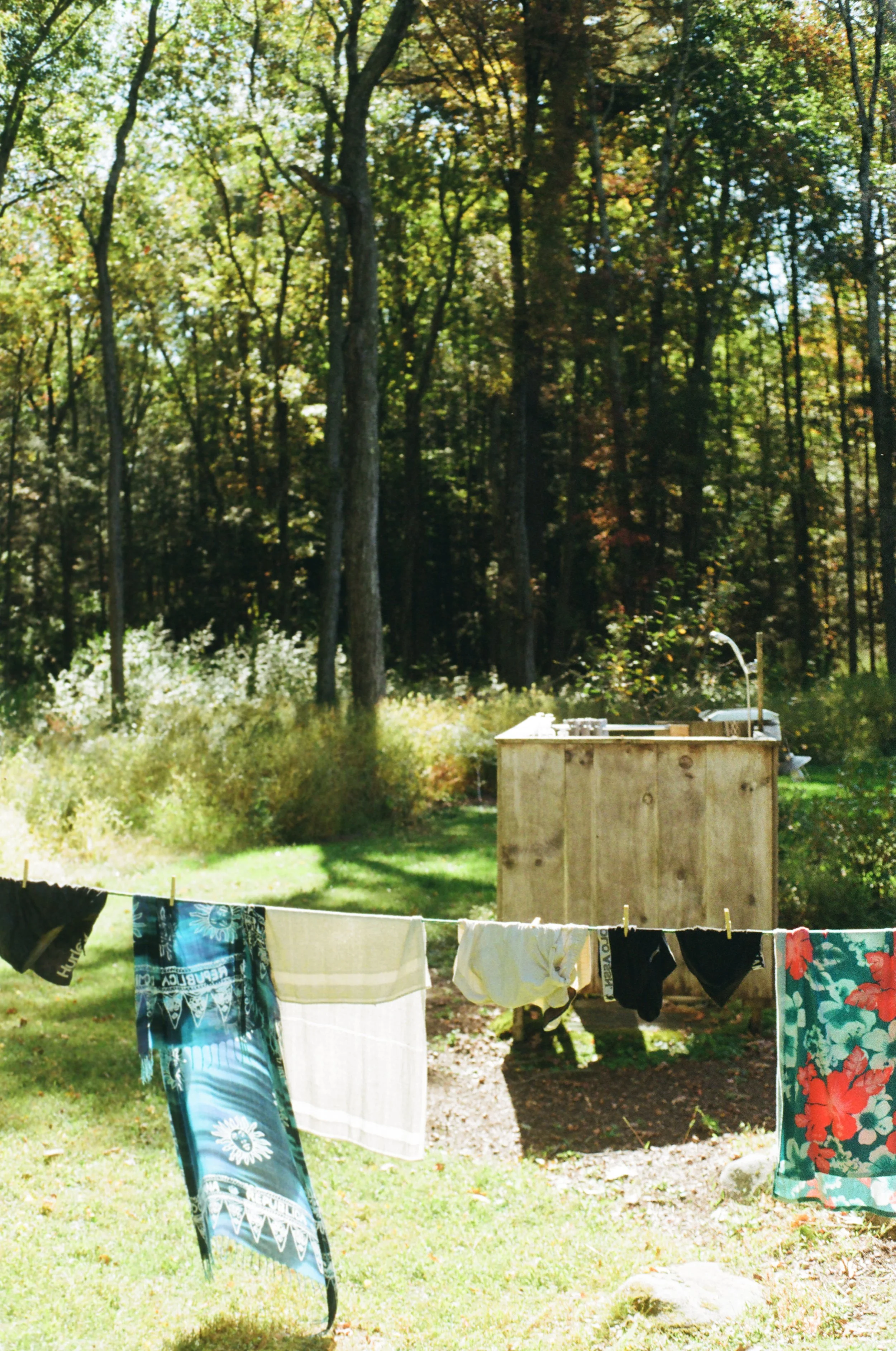 Laundry line with clothes hanging in a backyard with trees and a wooden outdoor sink.