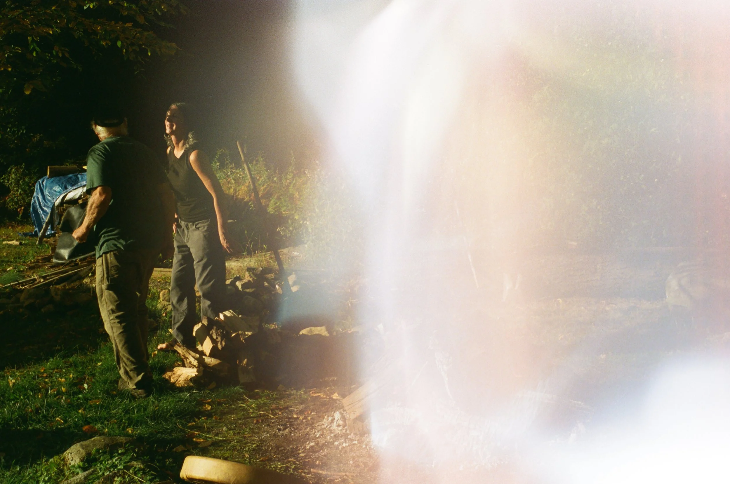 Two people outdoors, one man facing away and a woman standing, with a blurry light or reflection covering part of the right side of the image.