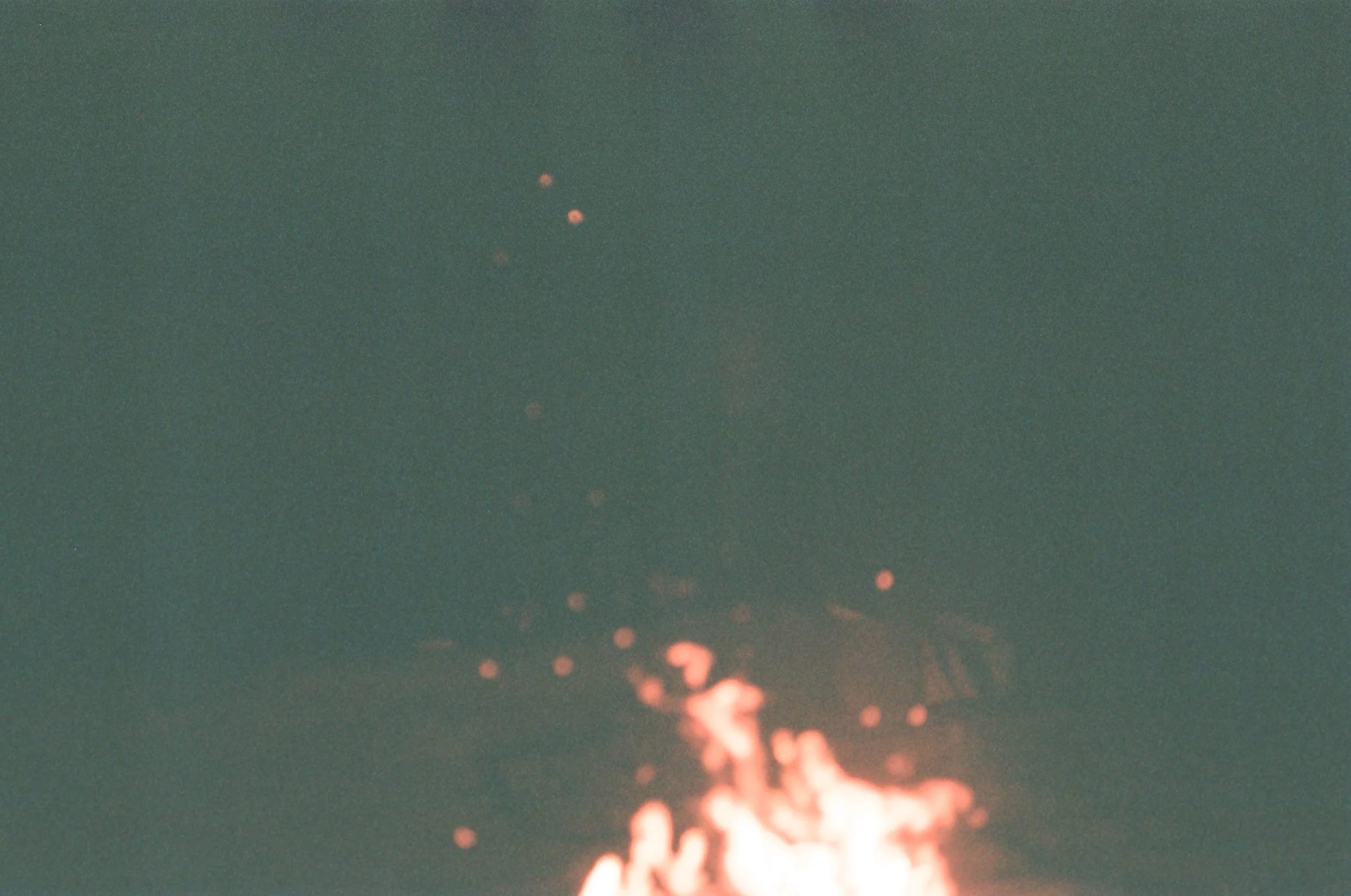 A fire burning at night with sparks flying into the dark sky.