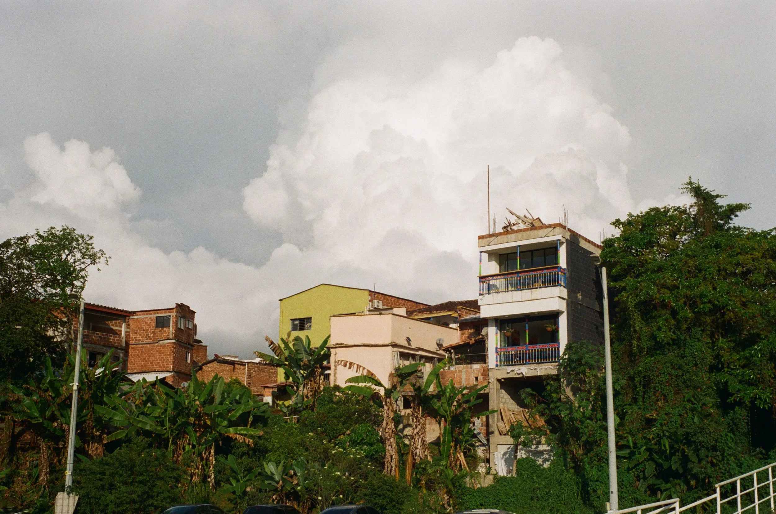Hilly neighborhood with colorful houses and lush green vegetation under a cloudy sky.