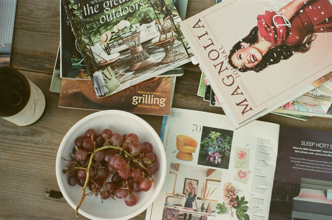 A table with a bowl of red grapes, a bottle, and several magazines and brochures spread out.
