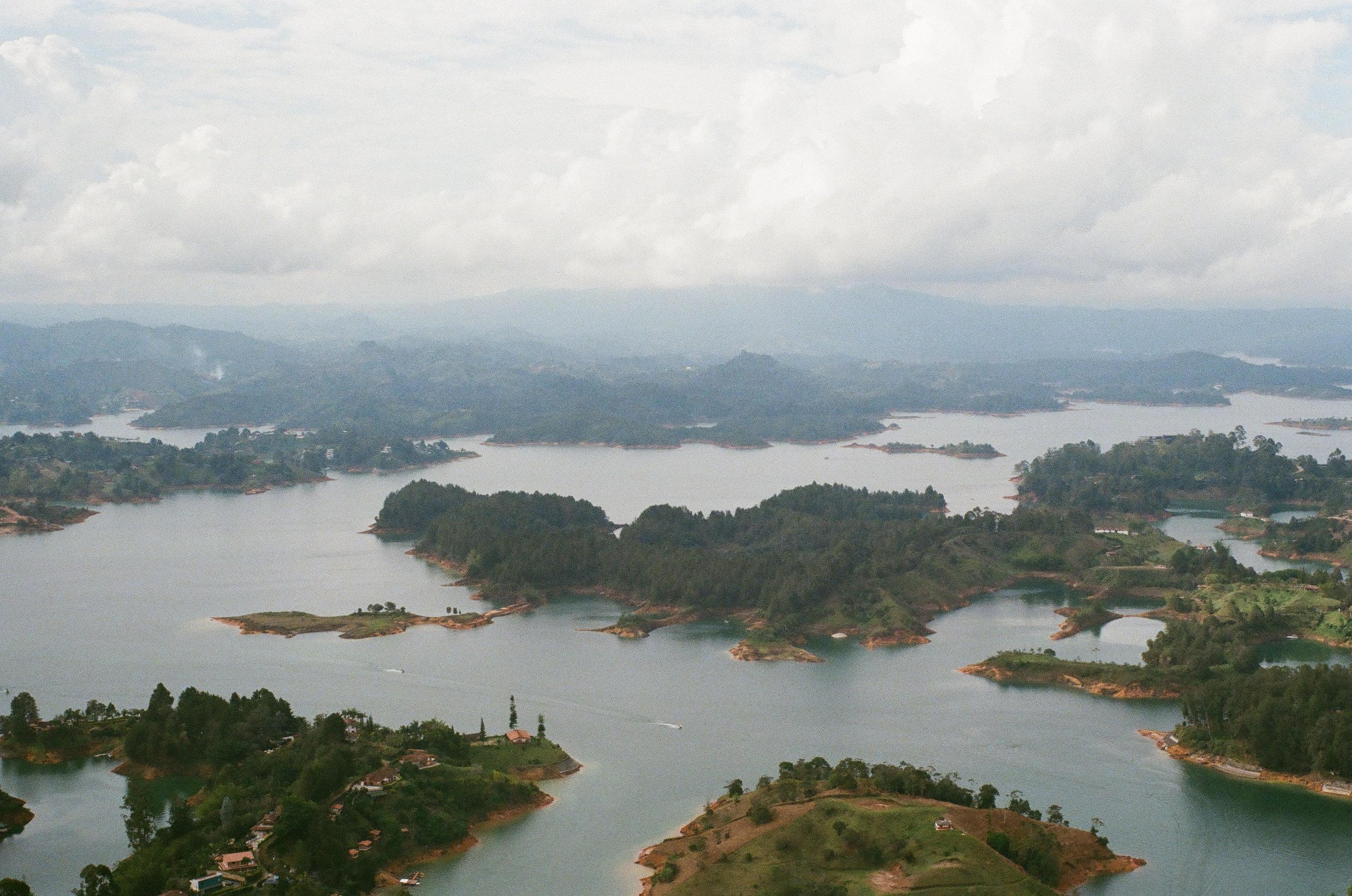 Aerial view of a lake with multiple islands and surrounding green hills under a cloudy sky.