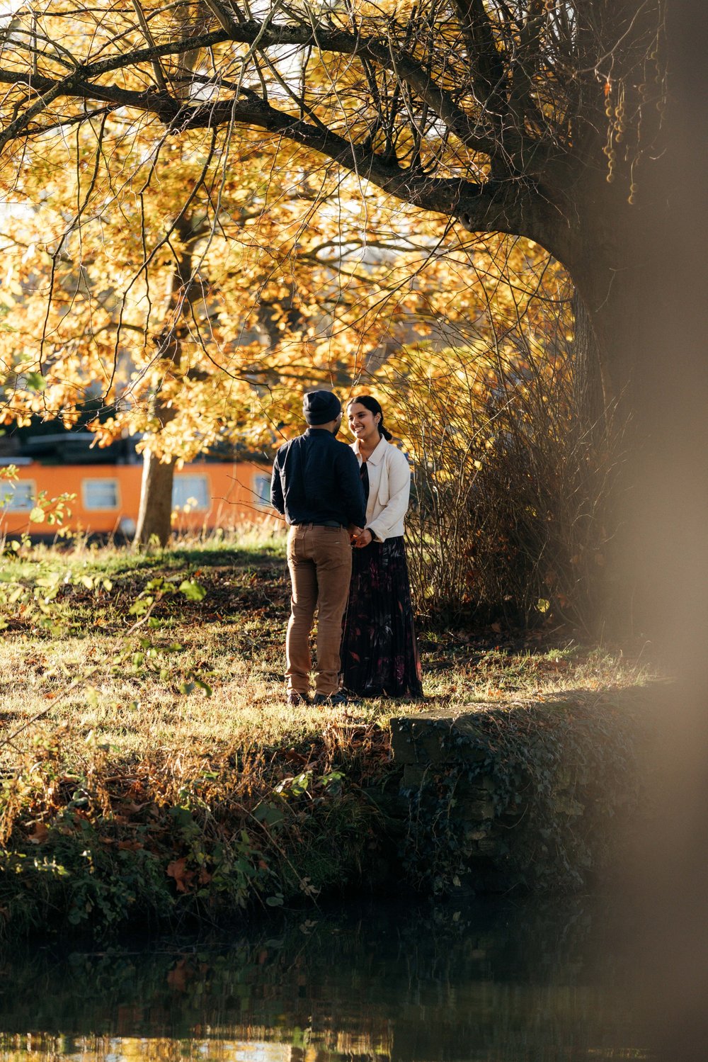 Engaged couple holding hands beside the water in autumn light