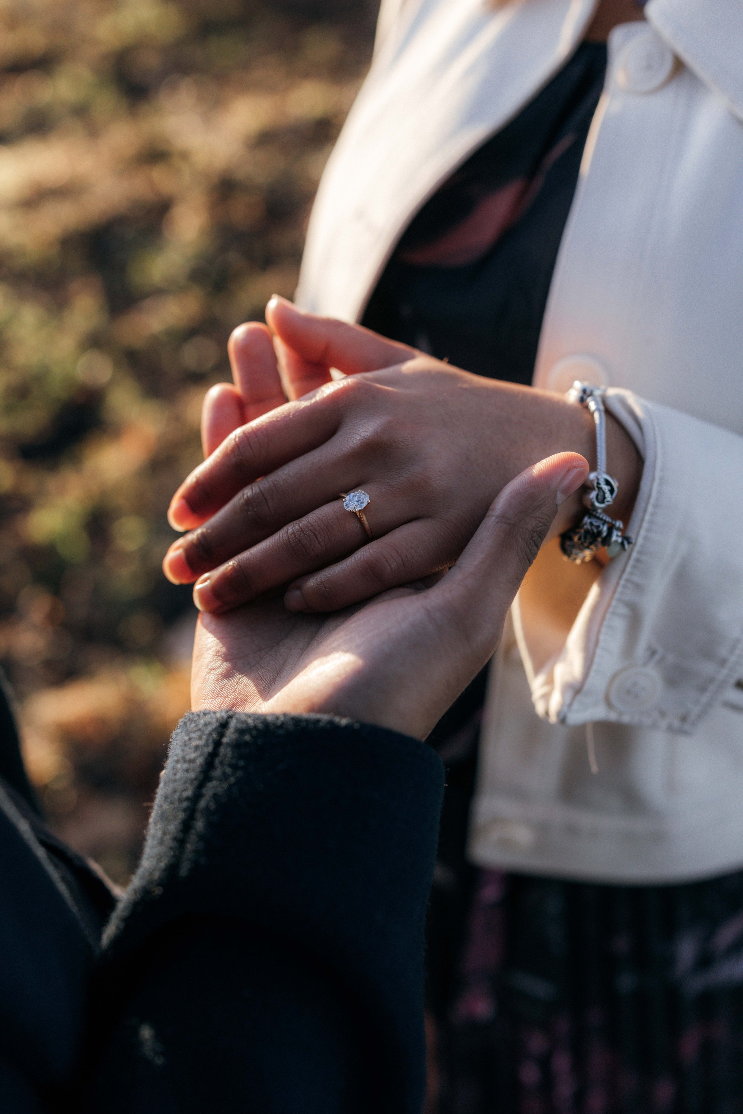 Close-up of a person placing their hand on top of another person's hand, showing an engagement ring on the finger.